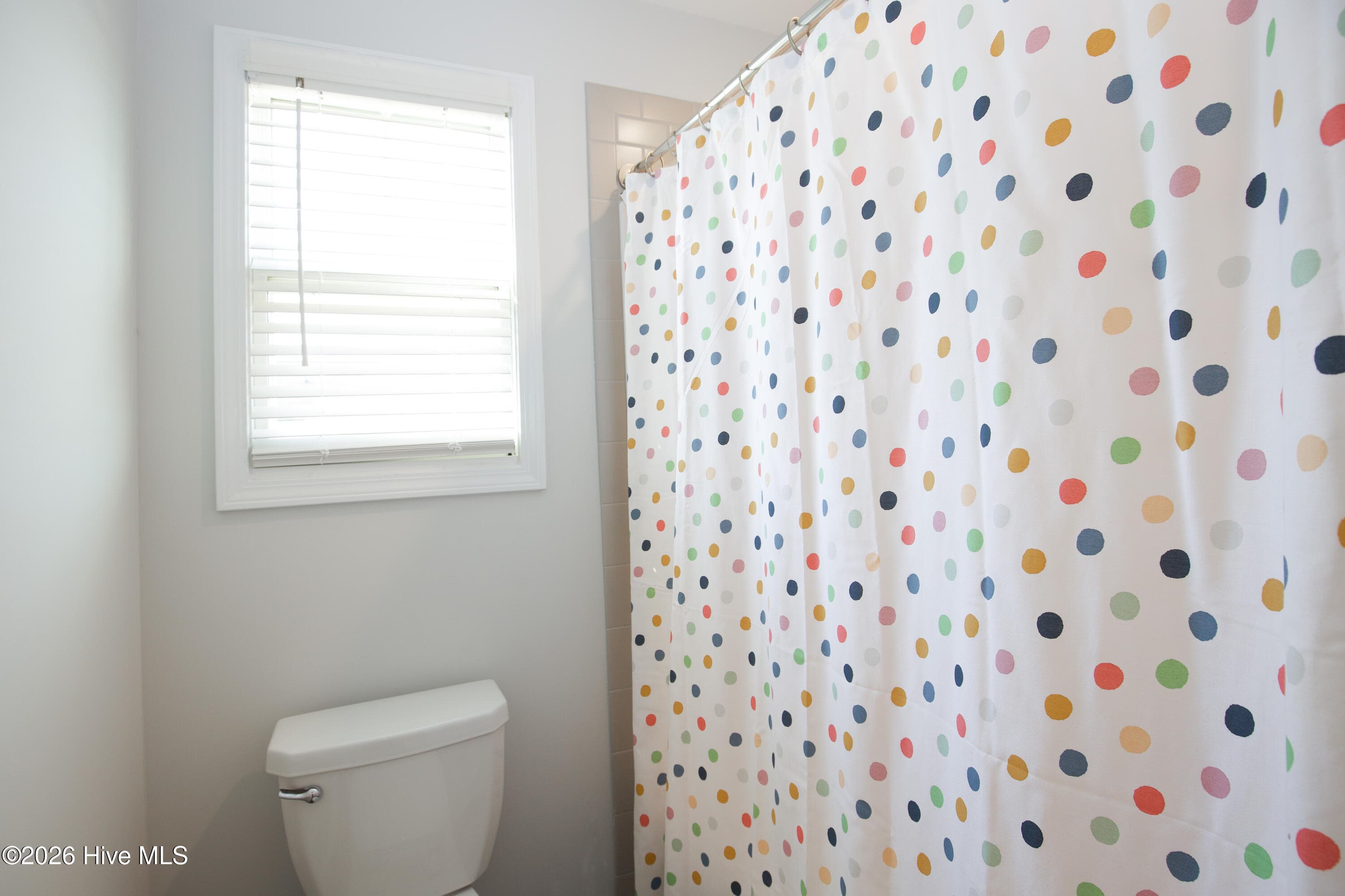 Behind the door in the hall bath, the toilet and tub/shower combination share their own space with a window for natural light. Keeping this area separate from the vanity adds privacy. A tile border is visible around the tub/shower surround. - 221 Vega Lane, Linden, NC 28356