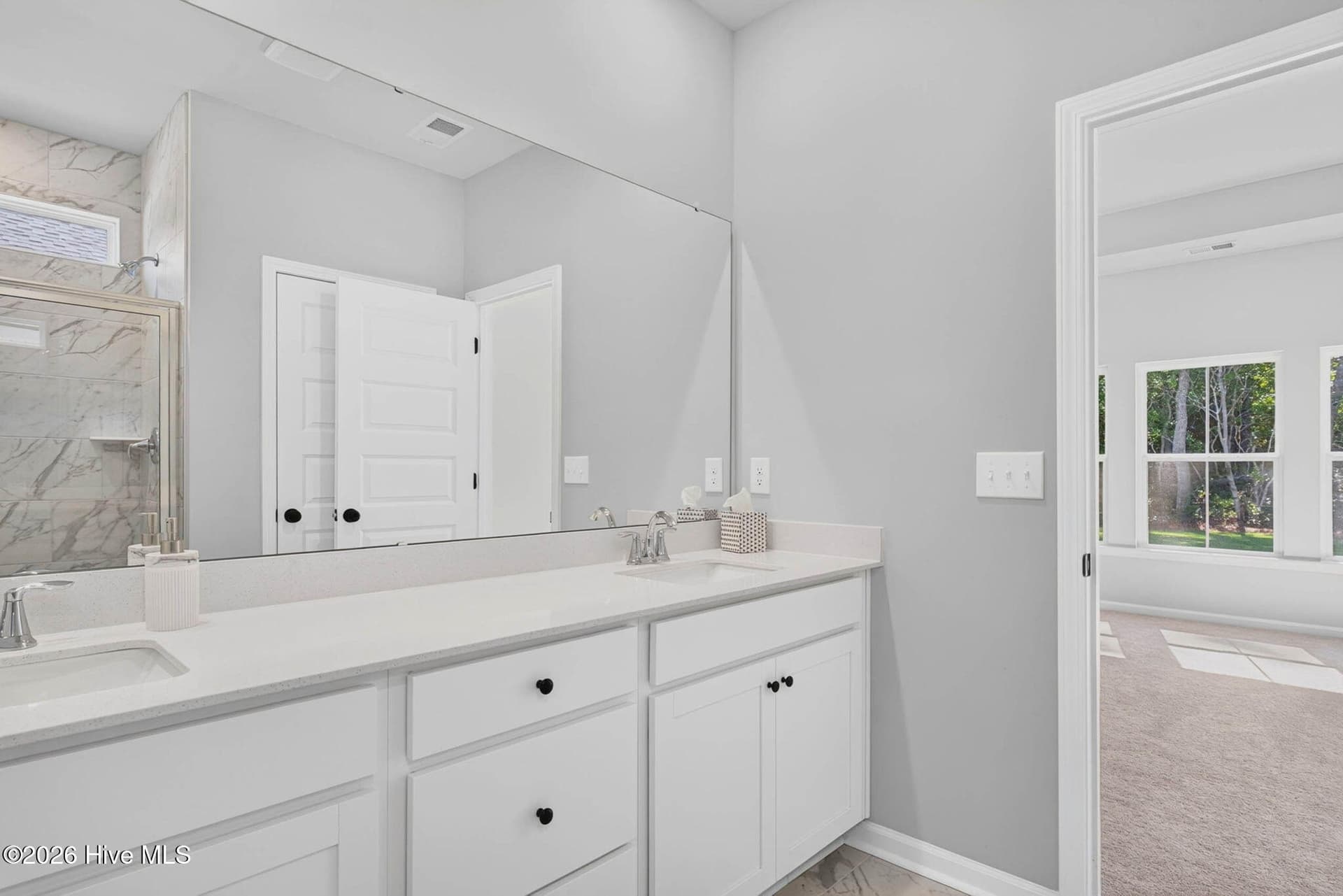 Additional view of the primary ensuite featuring double vanities, white cabinetry, and natural light. - 3447 Sandhill Crane Drive SW, Ocean Isle Beach, NC 28469