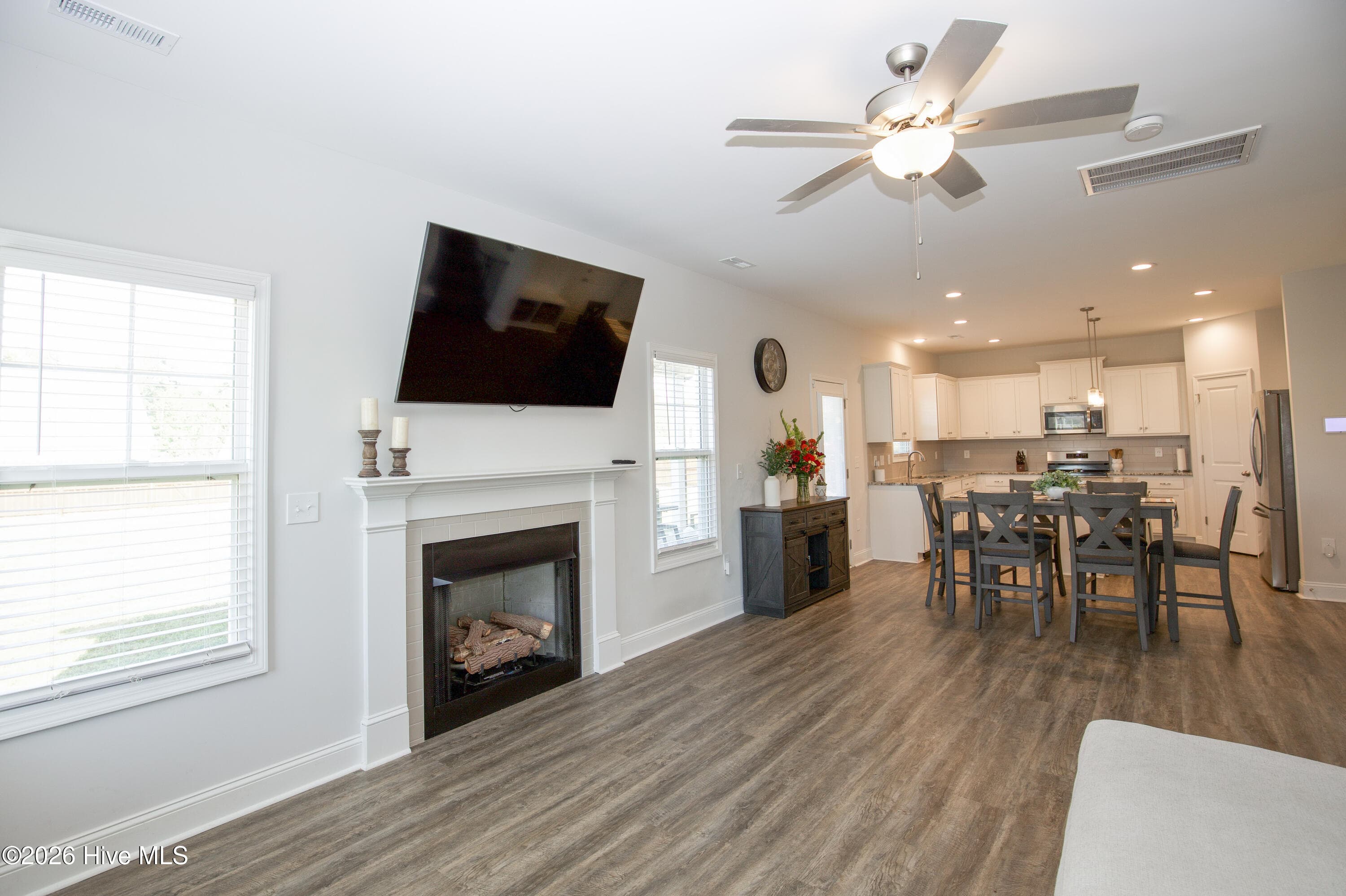 The Great Room centers on a fireplace with a white mantel and surround, flanked by windows on each side. Looking toward the back of the house, you can see the dining area and kitchen open to this room, which keeps the main level connected. The first floor has 9-foot ceilings according to the professional floor plan, adding to the sense of space. - 221 Vega Lane, Linden, NC 28356