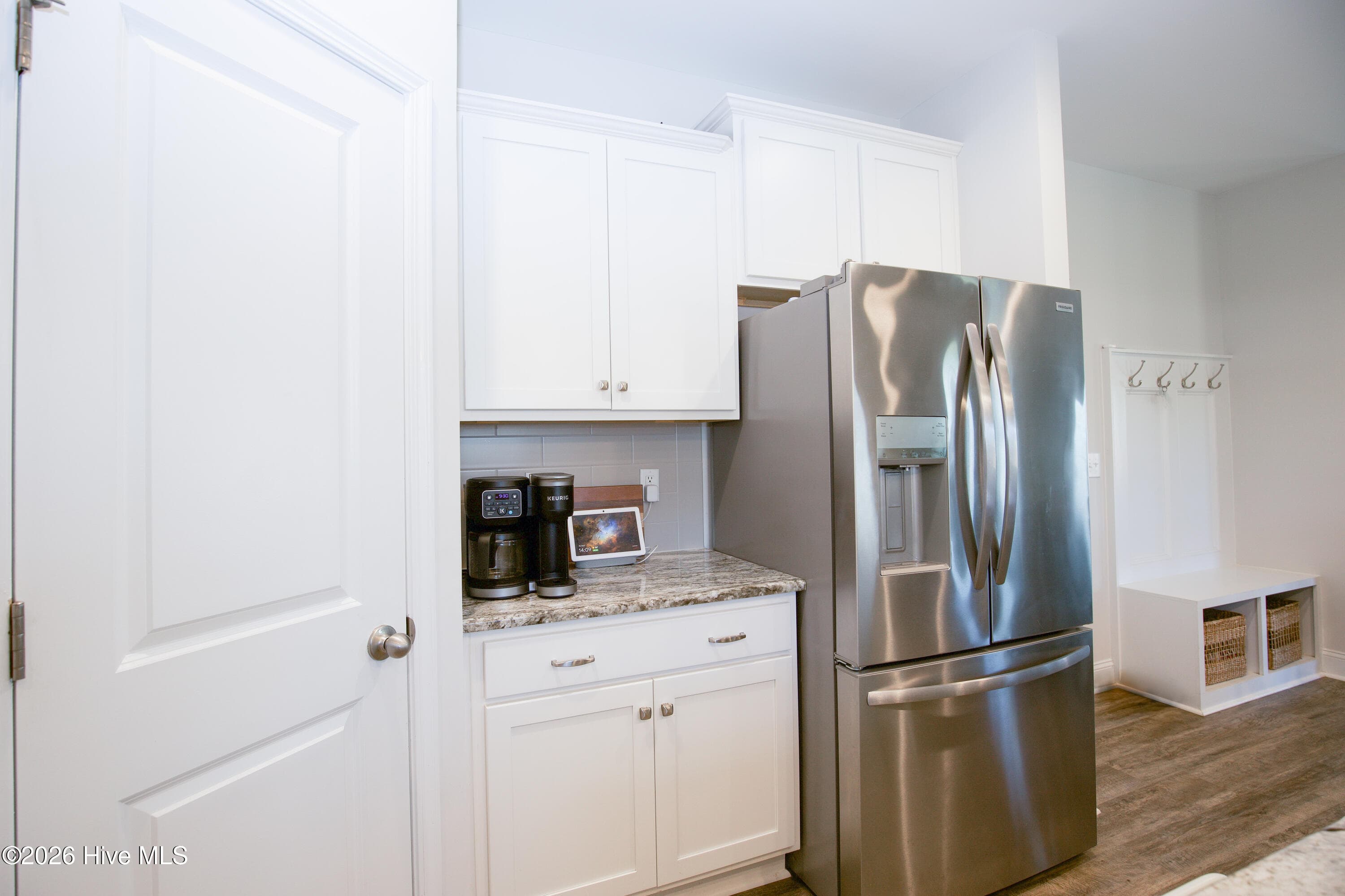 On the far side of the kitchen, a stainless French-door refrigerator sits beside a separate stretch of granite counter with cabinets above and below. This section works well as a coffee or beverage station, keeping that setup out of the main cooking area. The refrigerator conveys with the home, and the drop-zone bench with coat hooks is just around the corner. - 221 Vega Lane, Linden, NC 28356