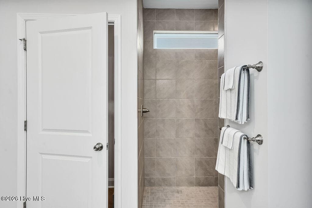 The owner's suite bathroom features spa-like details such as an upgraded L-shaped tiled shower, transom window upgrade, solar tube style sun tunnel, double sink vanity and two spacious walk-in closets. One of these passes through to the laundry room with its built-in folding station. - 142 Rice Marsh Way, Wilmington, NC 28412