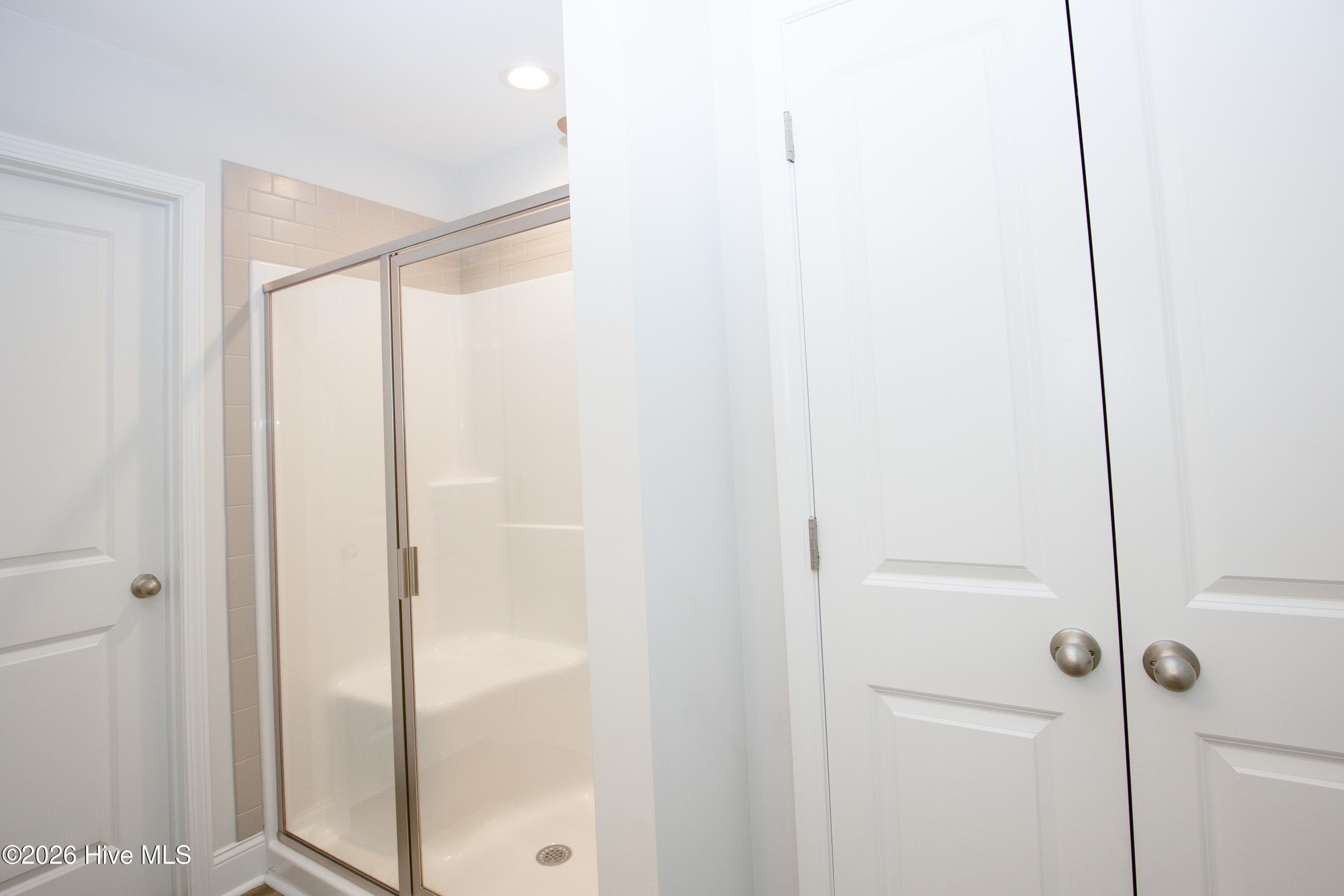 This side of the primary bath shows the glass-enclosed shower with tile above the surround, along with a double-door linen closet. The shower includes a built-in seat. Keeping towels and toiletries in the closet right beside the shower makes the bath easy to use day to day. - 221 Vega Lane, Linden, NC 28356