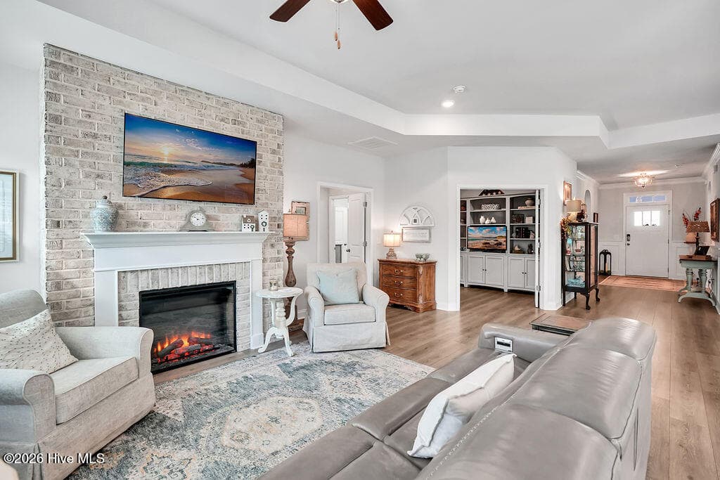 The living area is beautifully drenched in sunlight thanks to a bank of large, energy-efficient Low-E windows. Outfitted with custom plantation blinds, these windows allow for an easy transition between indoor and outdoor spaces and add an air of southern coastal charm to the neutral Scandi-meets-seaside color palette. A tray ceiling and an electric fireplace with custom brick surround complete this bright and open space. - 142 Rice Marsh Way, Wilmington, NC 28412