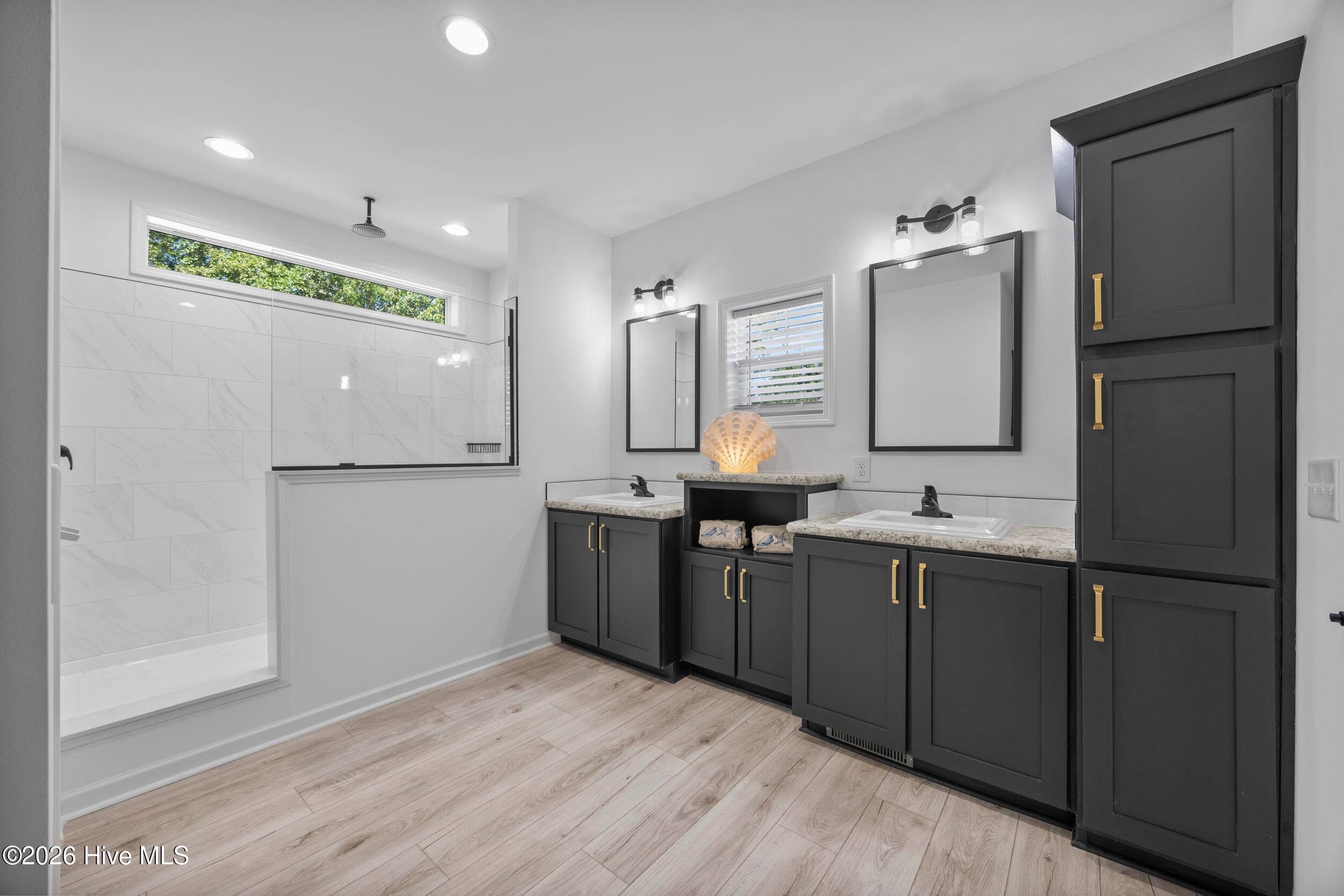 Spacious primary bathroom featuring an oversized walk-in shower, double sink vanity, elegant dark cabinetry, and generous storage. Modern finishes and abundant natural light create a bright and inviting retreat - 771 Factory Road, Hampstead, NC 28443