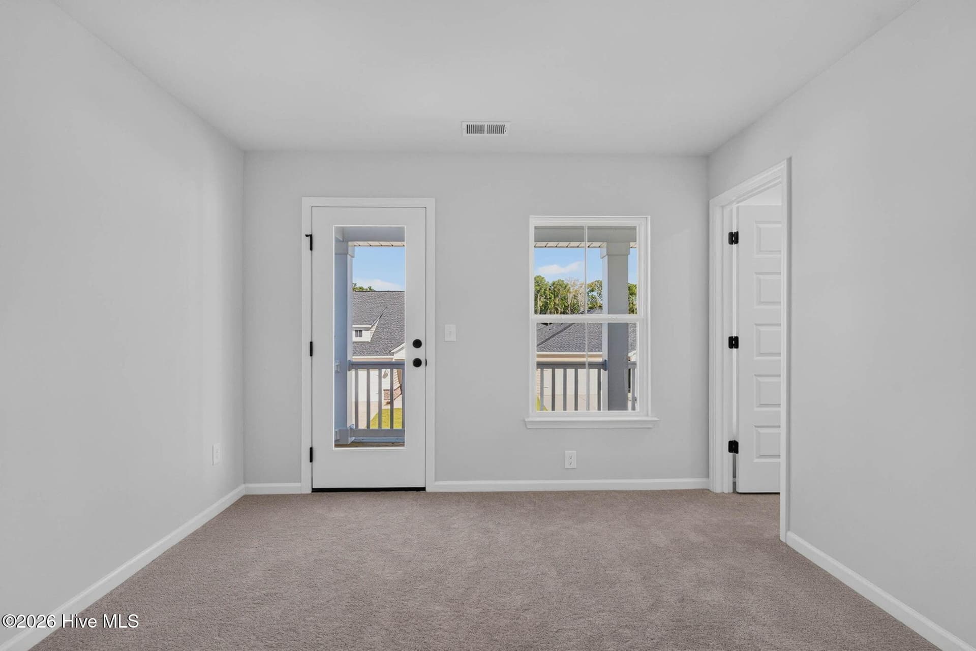 Bright upstairs bedroom featuring plush carpeting, natural light, and access to the covered balcony. - 3447 Sandhill Crane Drive SW, Ocean Isle Beach, NC 28469