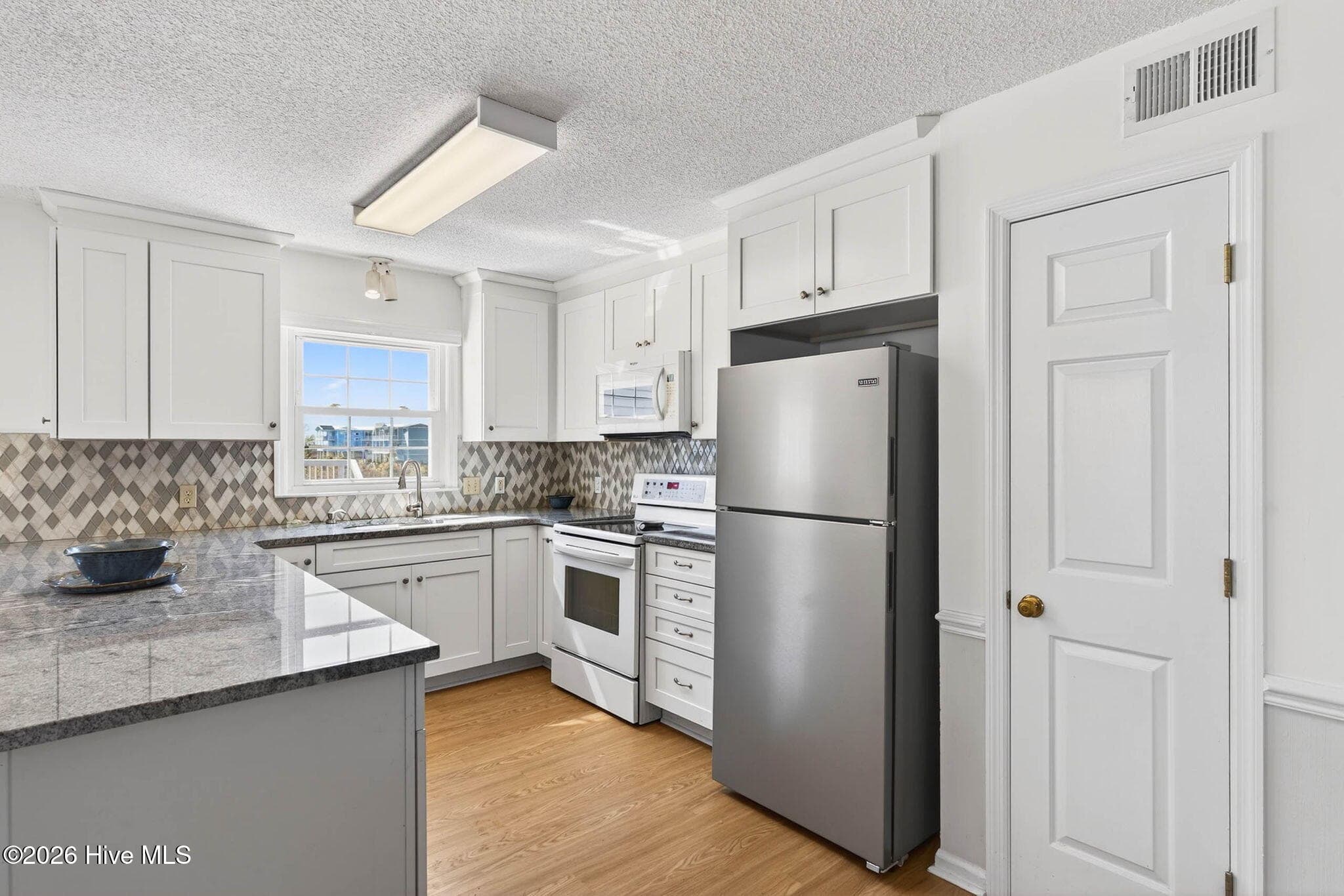 Fully equipped kitchen with stainless appliances, electric cooktop, and ample cabinetry. - 1206 N Shore Drive W, Sunset Beach, NC 28468