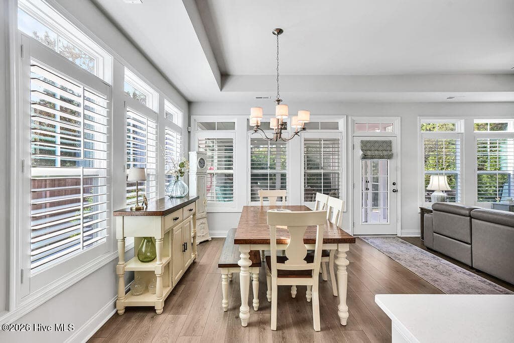 The dining area is absolutely drenched in sunlight thanks to a bank of large, energy-efficient Low-E windows. Outfitted with custom plantation blinds, these windows allow for an easy transition between indoor and outdoor spaces and add an air of southern coastal charm to the neutral Scandi-meets-seaside color palette. - 142 Rice Marsh Way, Wilmington, NC 28412