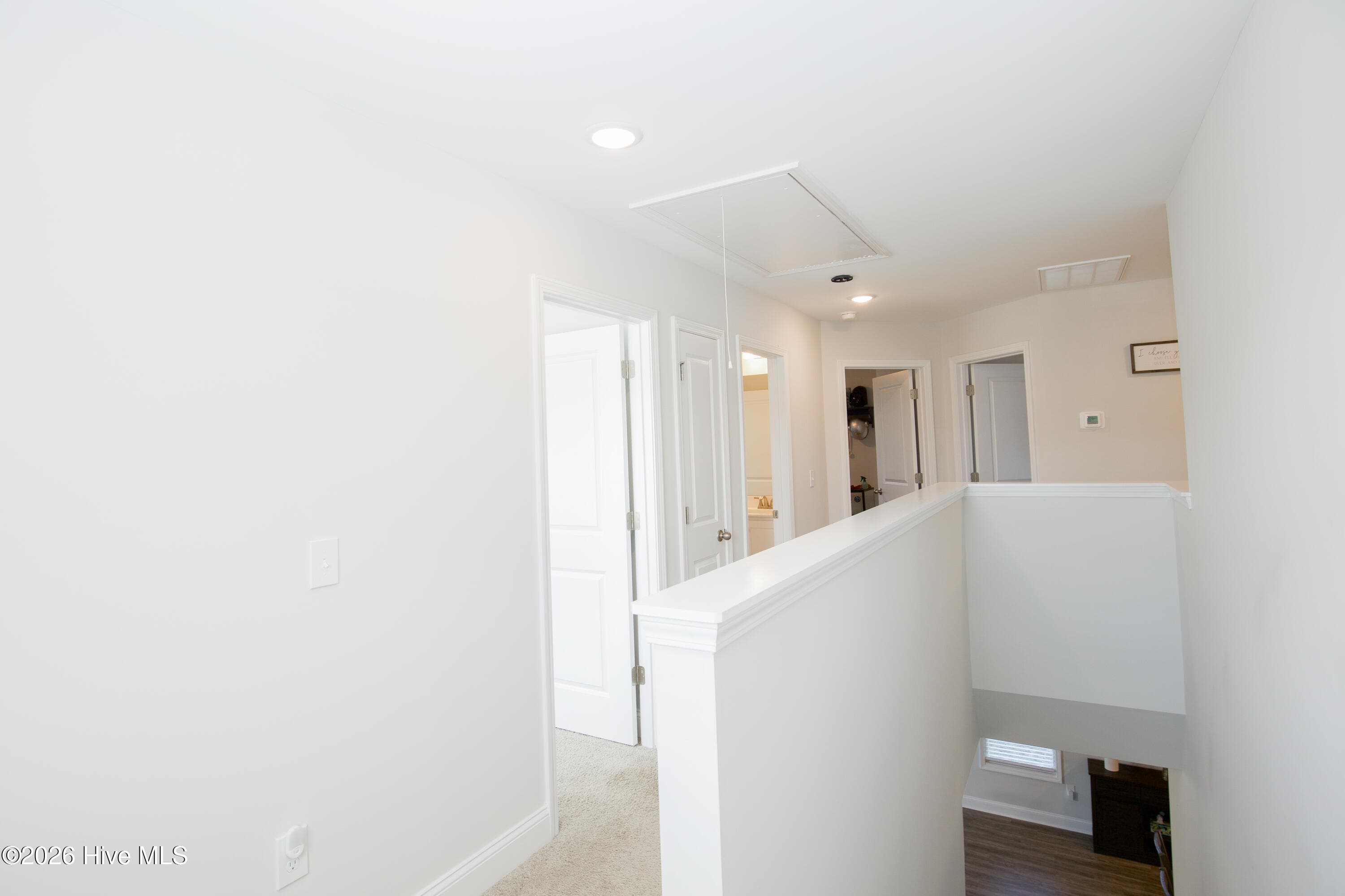 At the top of the stairs, a landing with a half wall overlooks the stairwell and connects to each of the upstairs rooms. All four bedrooms, the second full bath, and the laundry room are on this level. An attic access panel is visible in the hall ceiling. - 221 Vega Lane, Linden, NC 28356
