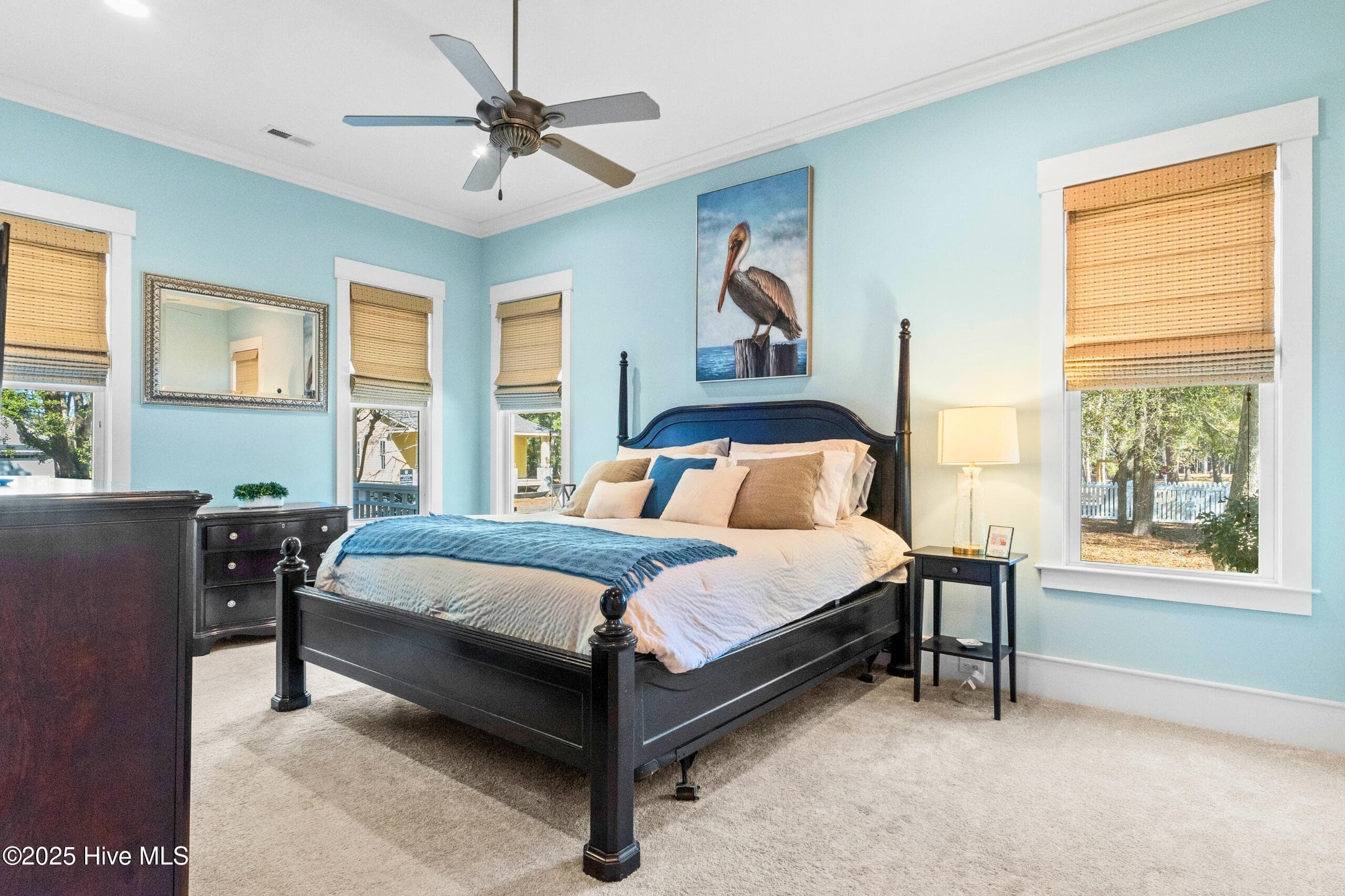 Main-level primary suite retreat featuring tray ceiling detail, ceiling fan, and direct access to private en-suite amenities. - 9100 Fountain Street SW, Calabash, NC 28467