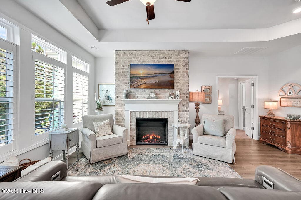 The living area is beautifully drenched in sunlight thanks to a bank of large, energy-efficient Low-E windows. Outfitted with custom plantation blinds, these windows allow for an easy transition between indoor and outdoor spaces and add an air of southern coastal charm to the neutral Scandi-meets-seaside color palette. A tray ceiling and an electric fireplace with custom brick surround complete this bright and open space. - 142 Rice Marsh Way, Wilmington, NC 28412