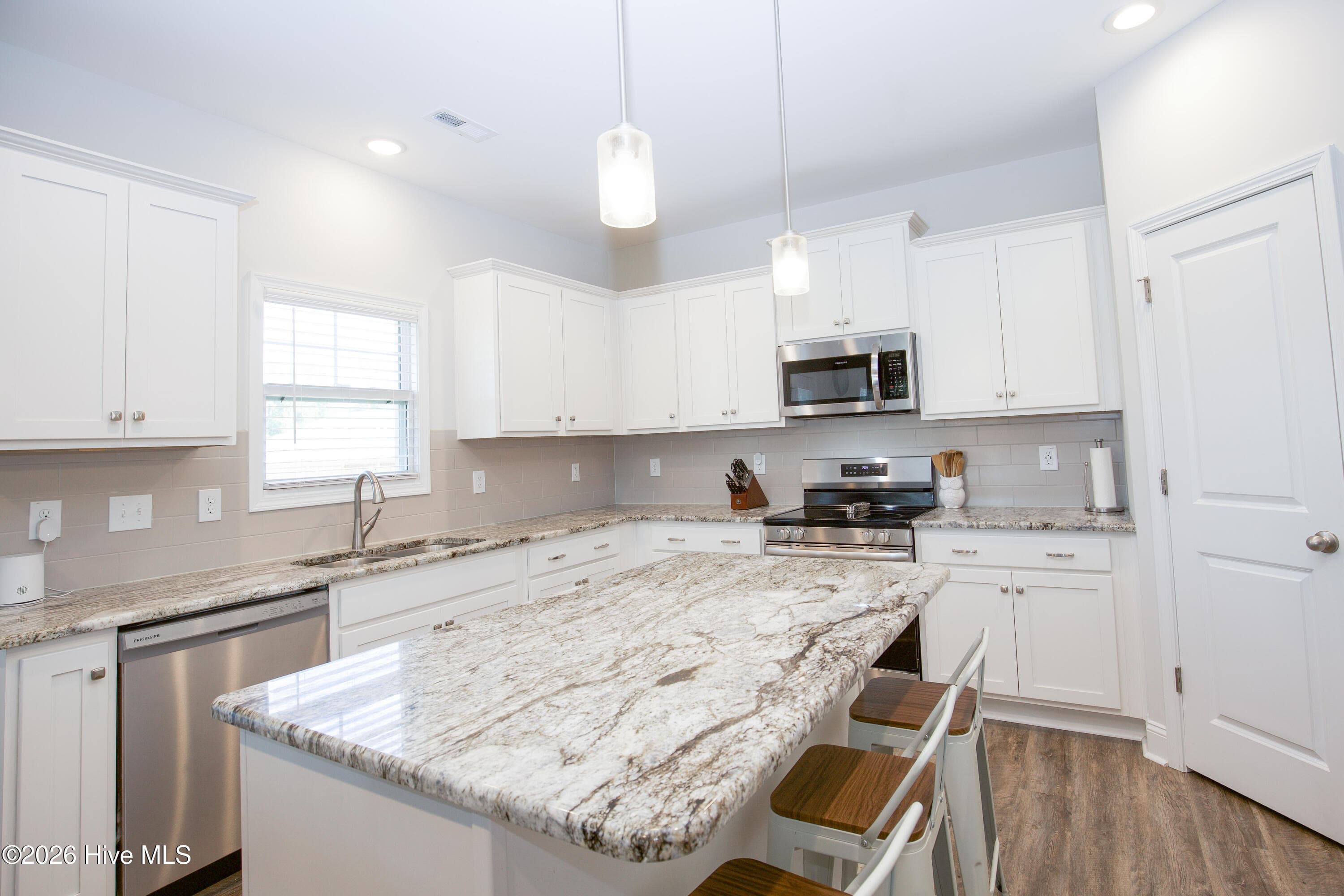 Seen from the end of the island, the kitchen opens up as one connected work area, with the sink under a window and the dishwasher right beside it. The island offers seating along one side, so someone can sit and visit while meals are being prepared. Natural light from the window above the sink brightens the white cabinetry and light granite. - 221 Vega Lane, Linden, NC 28356