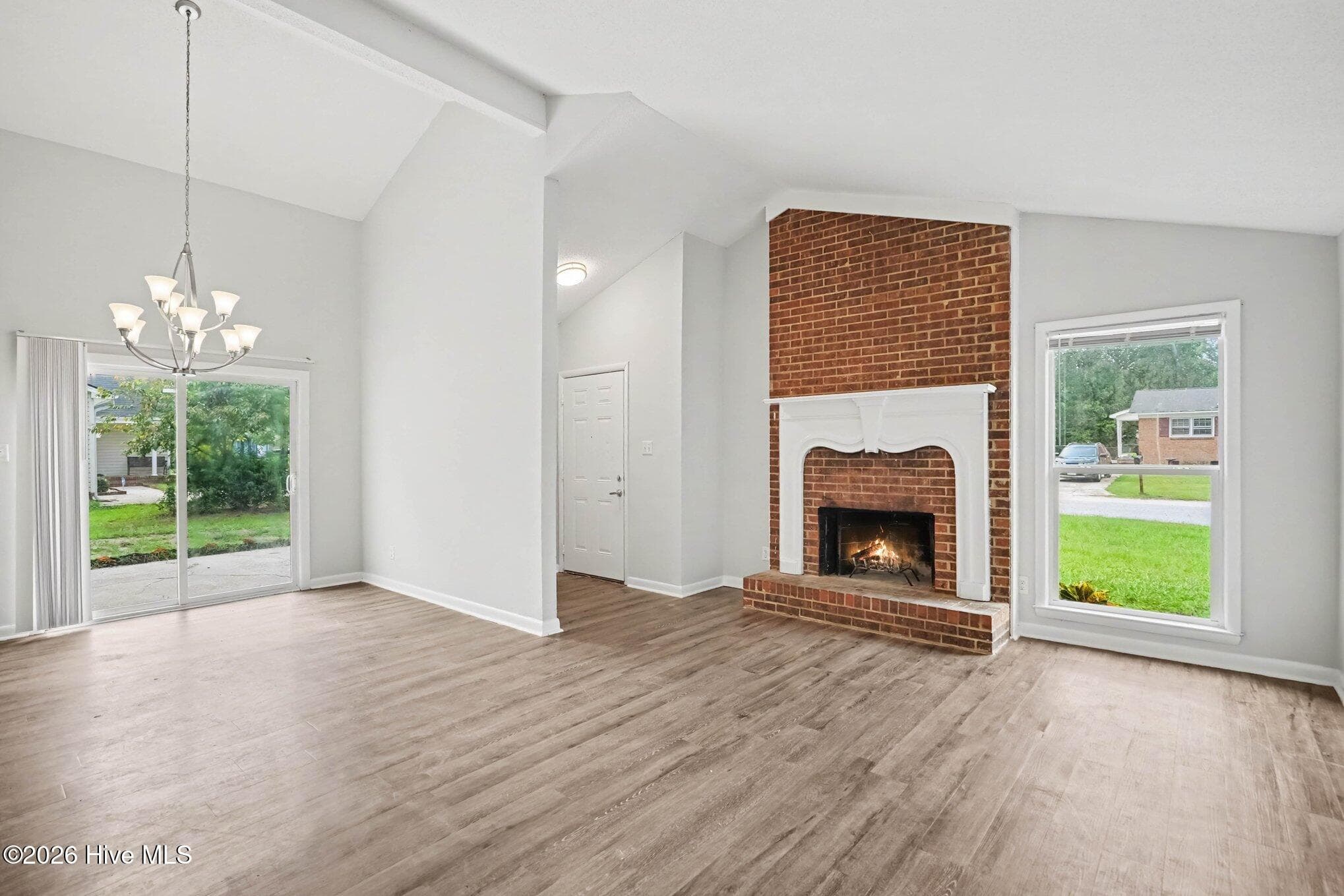Bright open-concept space featuring vaulted ceilings, wood tone vinyl plank flooring throughout. Front door is in the alcove next to the fireplace. - 108 Deerfield Drive, Spring Lake, NC 28390