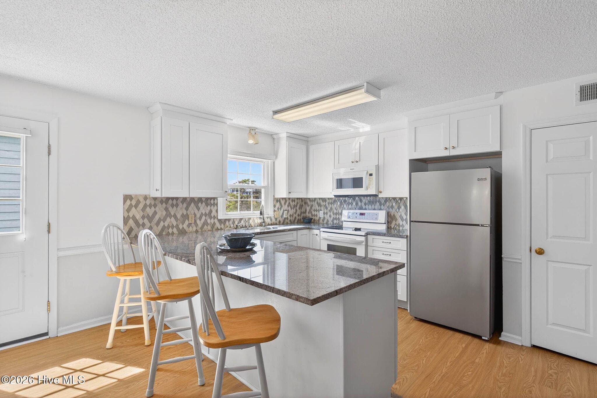 Updated kitchen with granite countertops, bar seating, and open layout for coastal living. - 1206 N Shore Drive W, Sunset Beach, NC 28468