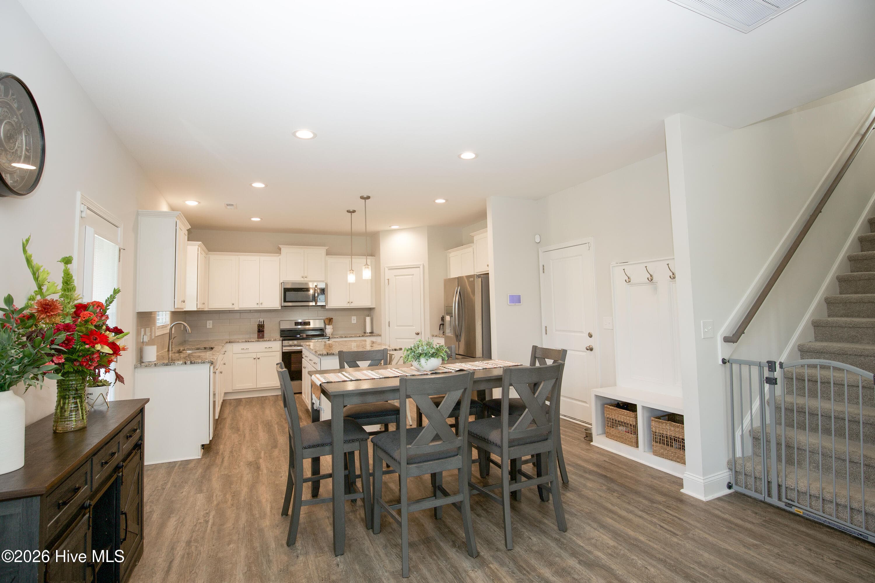 This view from the dining area shows how the main level is organized, with the kitchen ahead, the staircase to the right, and a built-in drop-zone bench with hooks near the door. The drop zone gives coats, bags, and shoes a dedicated spot so they do not end up on the kitchen counters. The stairs lead up to the four bedrooms and the upstairs laundry. - 221 Vega Lane, Linden, NC 28356