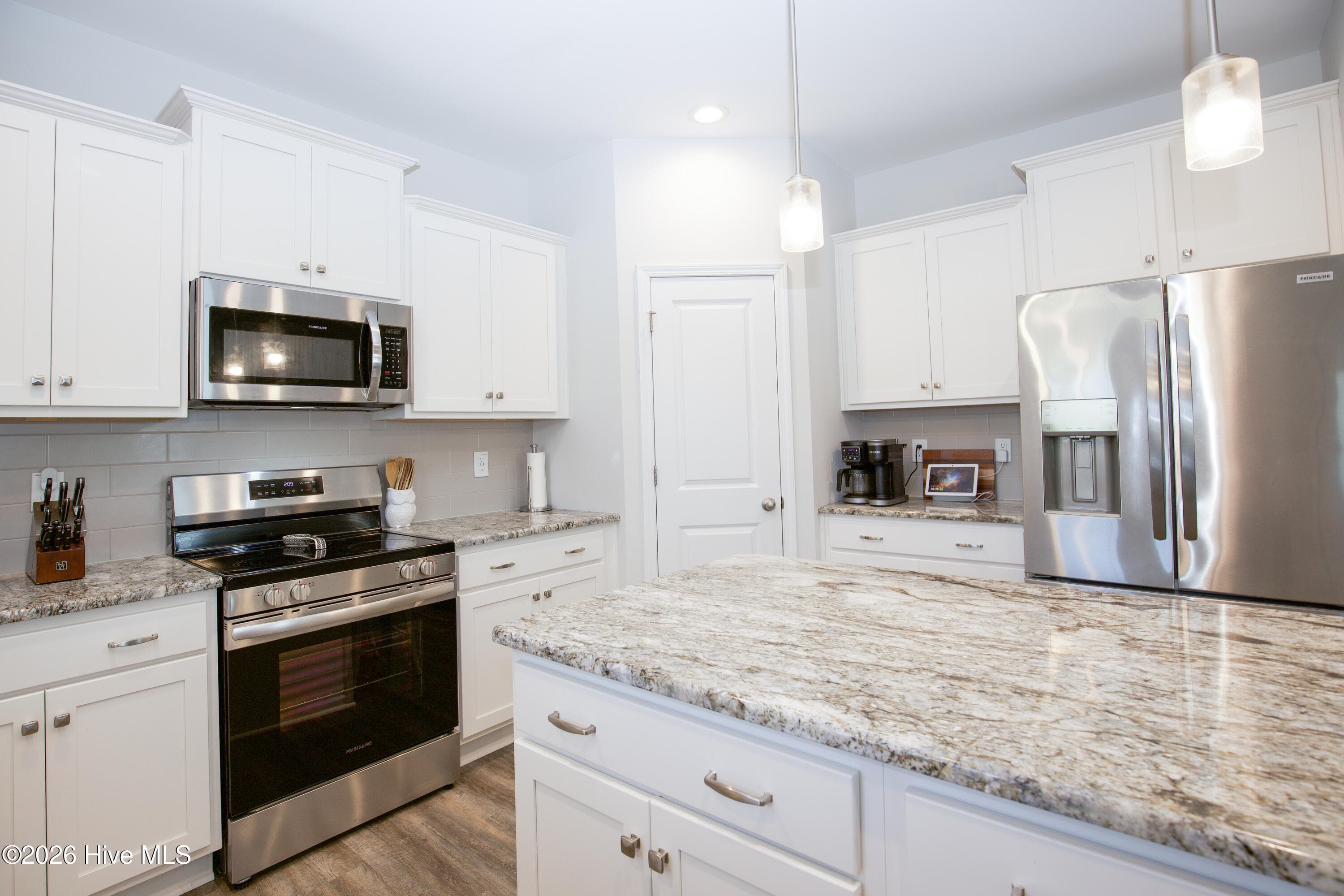 This angle shows the cooking side of the kitchen, with a stainless smooth-top electric range and an over-range microwave set between upper and lower cabinets. The island's granite top sits just a step away, which makes it easy to move from stove to prep area. A door beside the refrigerator leads to the pantry shown on the floor plan. - 221 Vega Lane, Linden, NC 28356