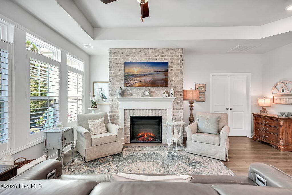 The living area is beautifully drenched in sunlight thanks to a bank of large, energy-efficient Low-E windows. Outfitted with custom plantation blinds, these windows allow for an easy transition between indoor and outdoor spaces and add an air of southern coastal charm to the neutral Scandi-meets-seaside color palette. A tray ceiling and an electric fireplace with custom brick surround complete this bright and open space. - 142 Rice Marsh Way, Wilmington, NC 28412