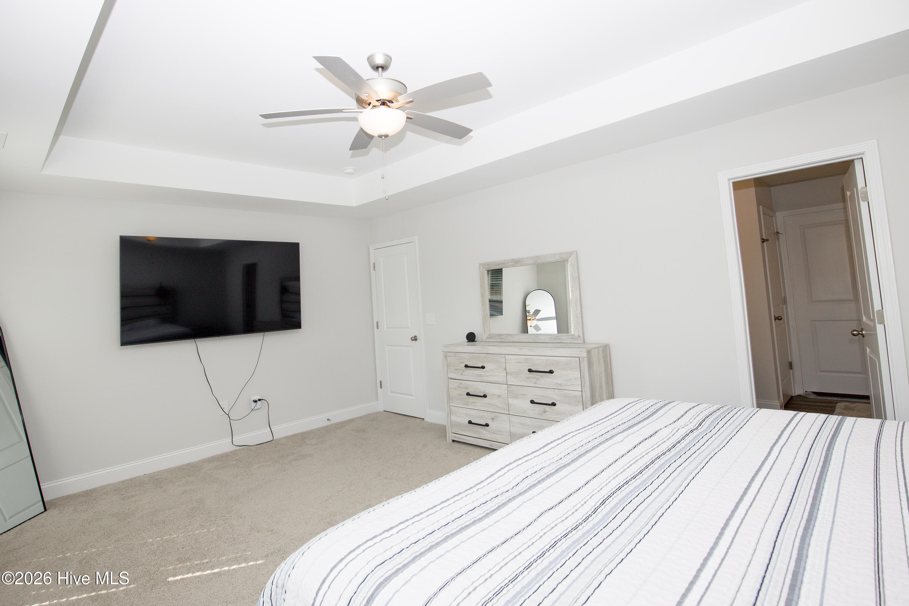 Stepping into the primary suite, you see a tray ceiling with a ceiling fan above the bed area and wall space for a dresser and a television. The doorway to the private bath and walk-in closet is on the right. The primary suite is located at the front of the second floor according to the floor plan. - 221 Vega Lane, Linden, NC 28356