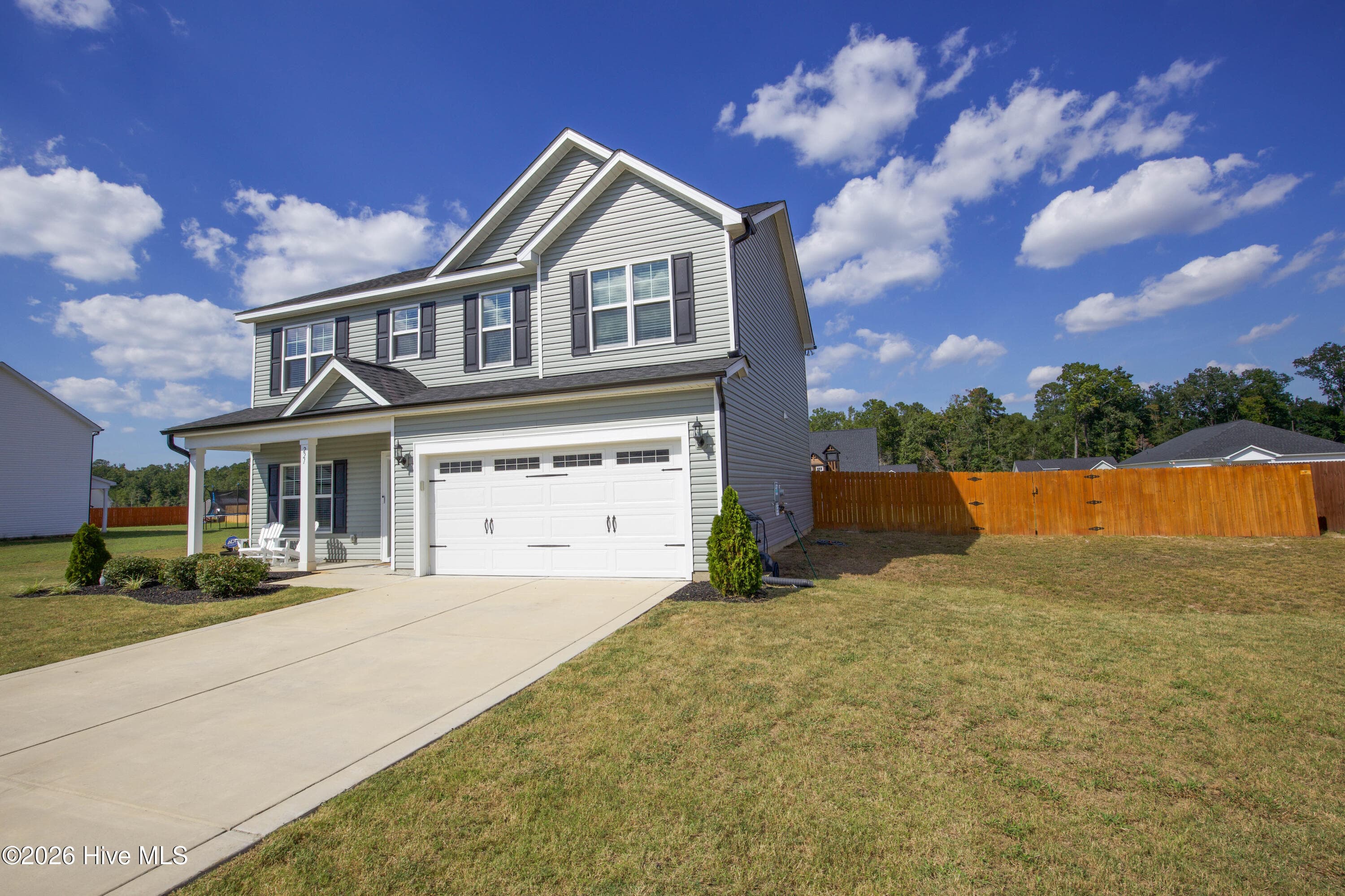 The rear of the house shows the covered patio centered on the back wall and the privacy fence running out from each side of the home. A wide stretch of mostly level lawn separates the house from the back fence line. This view gives a clear sense of how much usable outdoor space comes with the home. - 221 Vega Lane, Linden, NC 28356