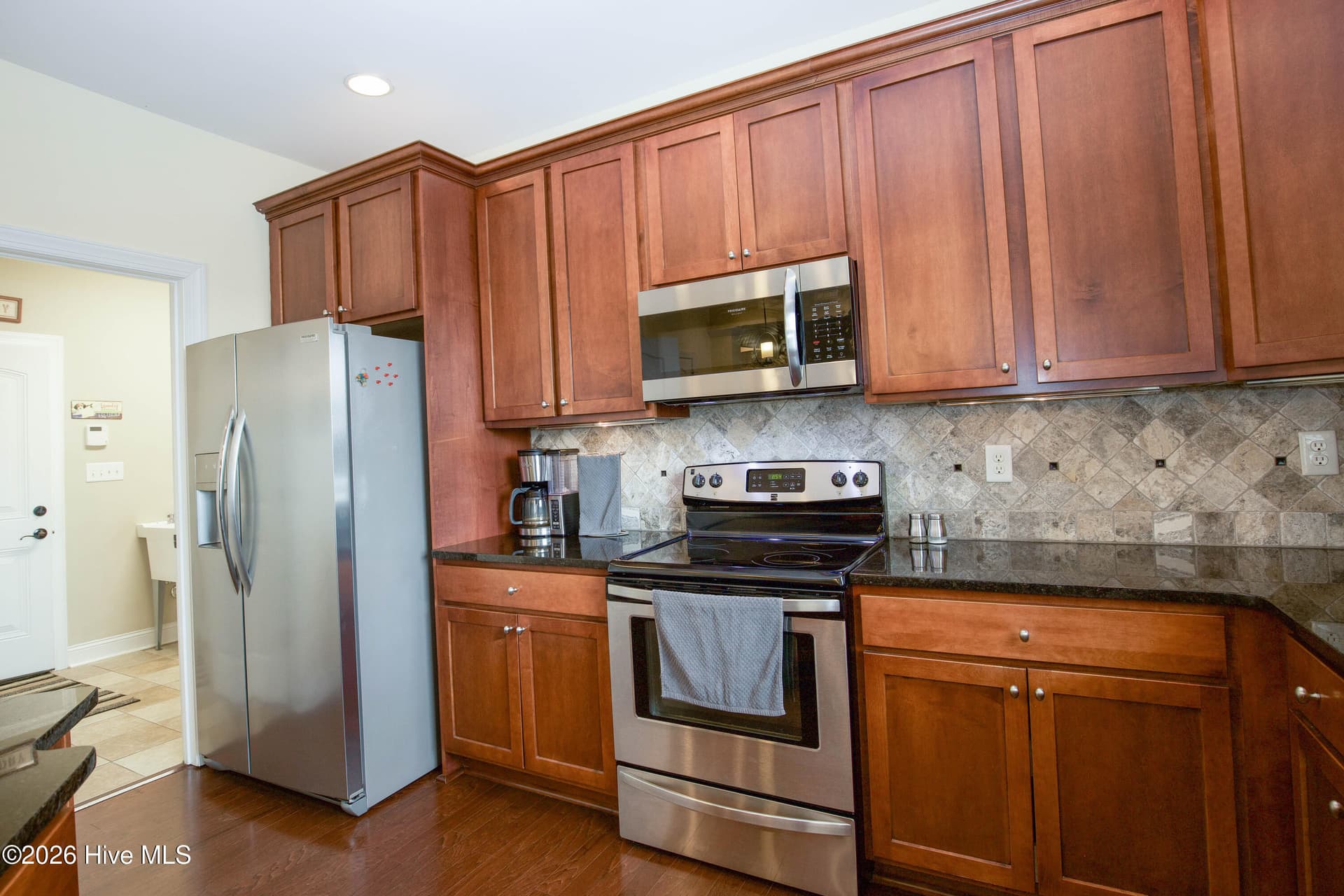 Kitchen with stainless refrigerator, range, and microwave and a tile backsplash. - 899 Seagull Drive, Vass, NC 28394