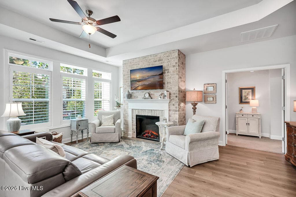 The living area is beautifully drenched in sunlight thanks to a bank of large, energy-efficient Low-E windows. Outfitted with custom plantation blinds, these windows allow for an easy transition between indoor and outdoor spaces and add an air of southern coastal charm to the neutral Scandi-meets-seaside color palette. A tray ceiling and an electric fireplace with custom brick surround complete this bright and open space. - 142 Rice Marsh Way, Wilmington, NC 28412