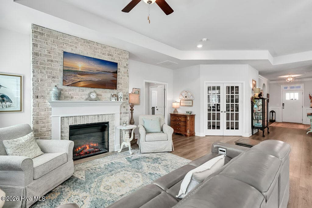 The living area is beautifully drenched in sunlight thanks to a bank of large, energy-efficient Low-E windows. Outfitted with custom plantation blinds, these windows allow for an easy transition between indoor and outdoor spaces and add an air of southern coastal charm to the neutral Scandi-meets-seaside color palette. A tray ceiling and an electric fireplace with custom brick surround complete this bright and open space. - 142 Rice Marsh Way, Wilmington, NC 28412