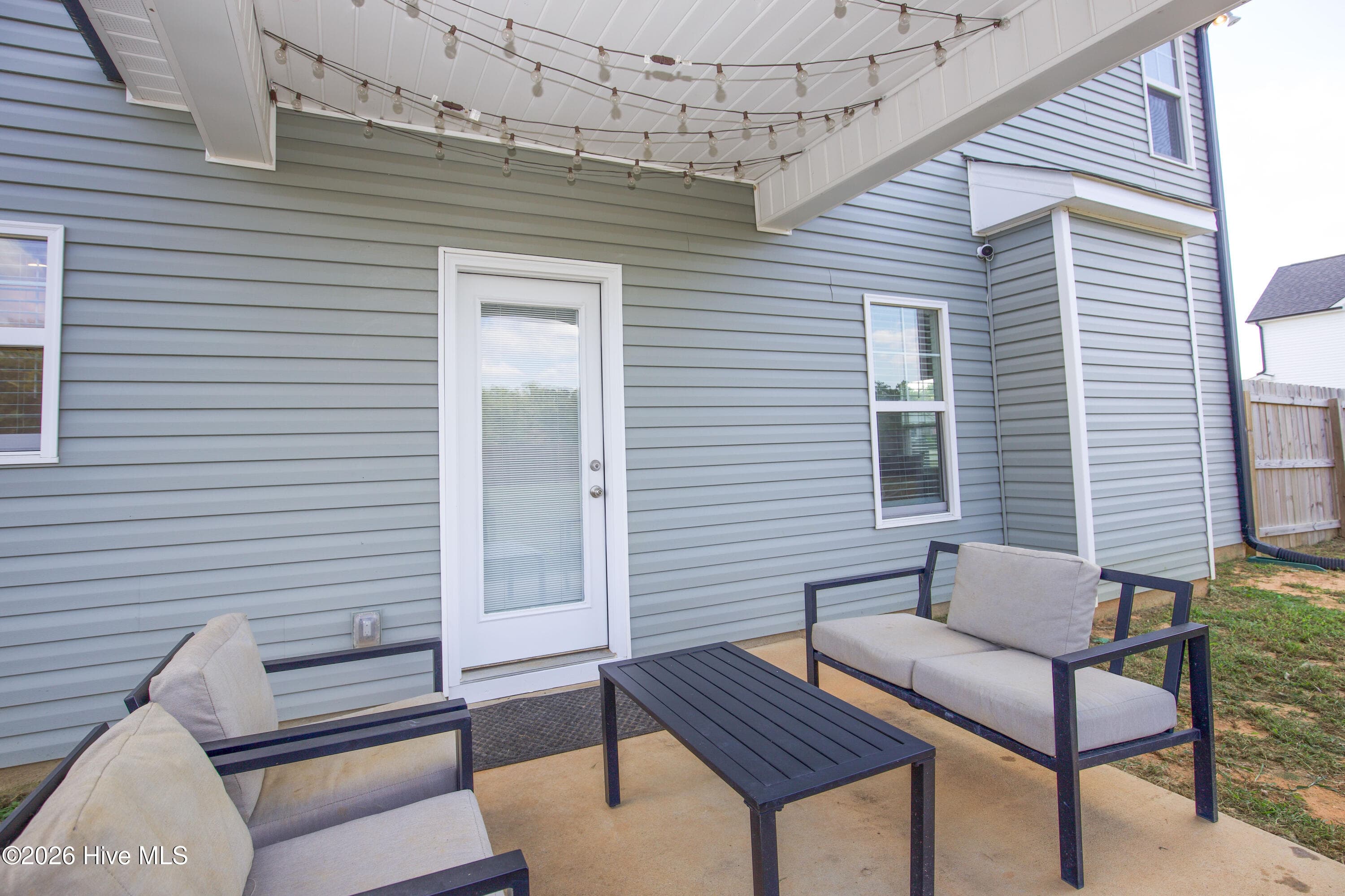 From the yard side, the rear door opens directly onto the covered patio, connecting the kitchen and dining area to the outdoor space. Vinyl siding and a rear window are visible, along with the patio's concrete pad. The setup makes it easy to bring meals outside or keep an eye on the yard from indoors. - 221 Vega Lane, Linden, NC 28356