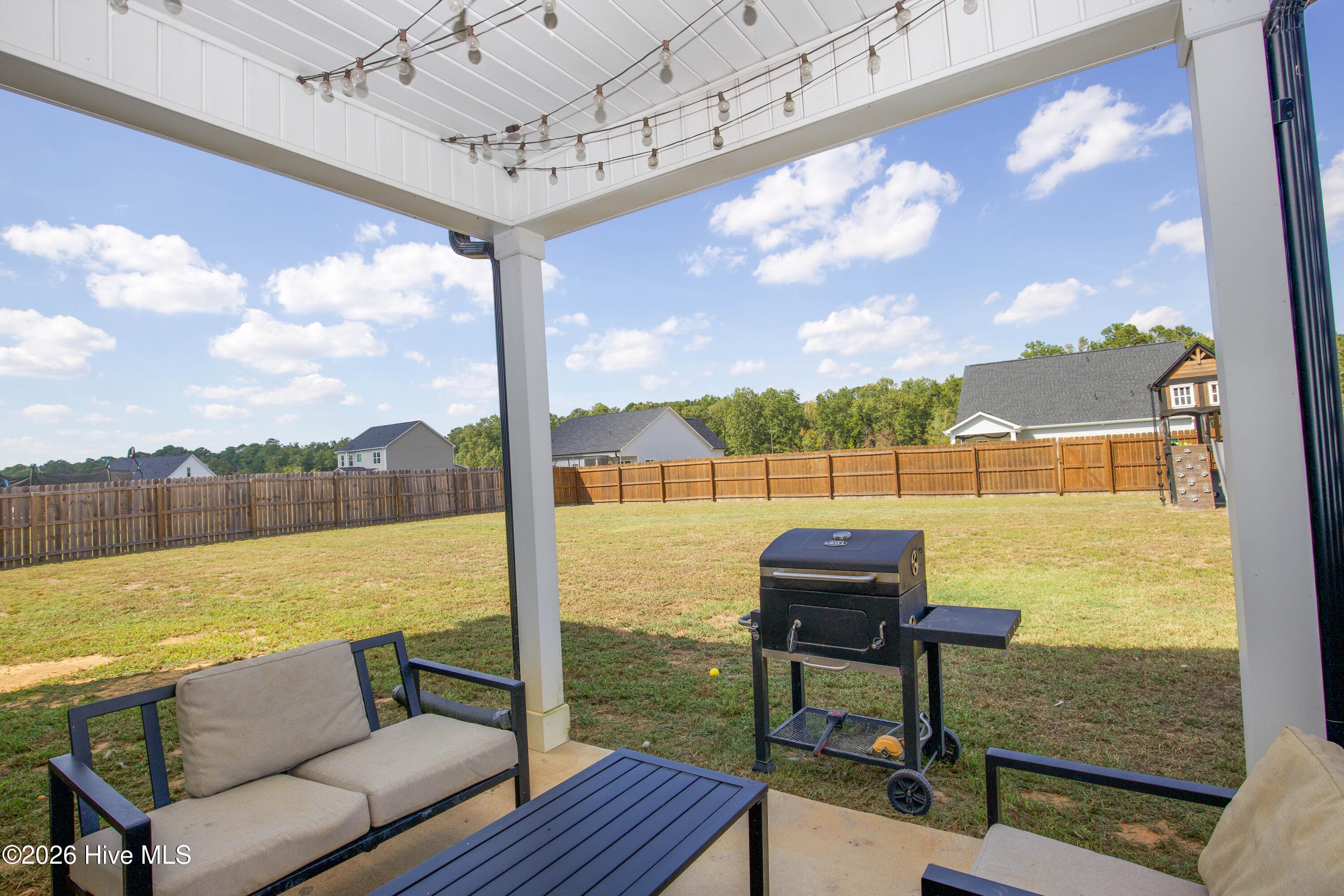 Sitting under the patio roof, you look out across the open backyard to the wood privacy fence and the playground equipment at the back. The yard offers plenty of open lawn for outdoor use. Having a covered space attached to the house means you can sit outside in light rain or summer sun. - 221 Vega Lane, Linden, NC 28356