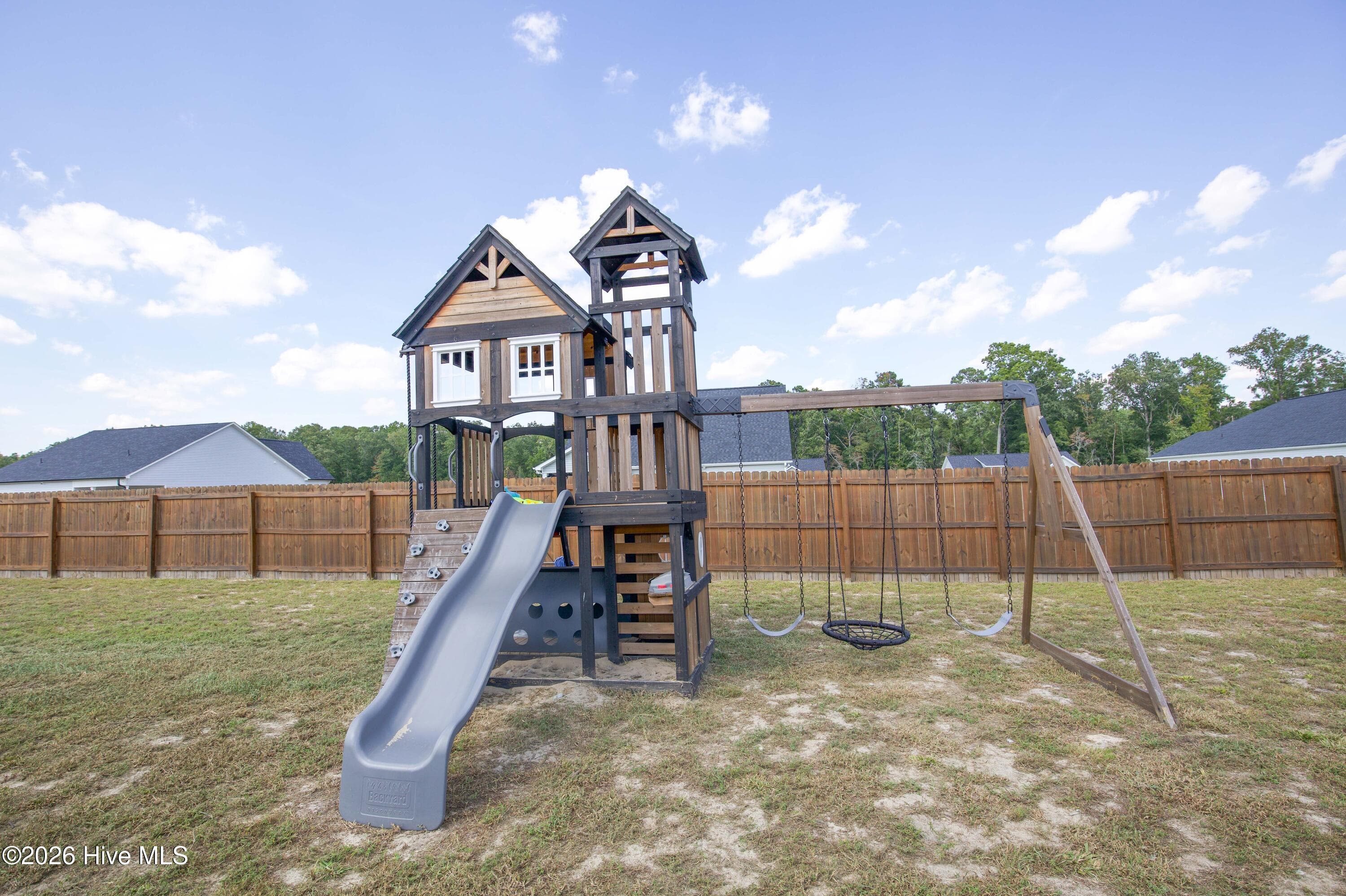 The backyard playground equipment includes a two-tower play structure with a slide, climbing wall, and swing set. It conveys with the property, so the yard is ready to use from the day you move in. The equipment sits inside the fenced backyard on a mostly level area of lawn. - 221 Vega Lane, Linden, NC 28356
