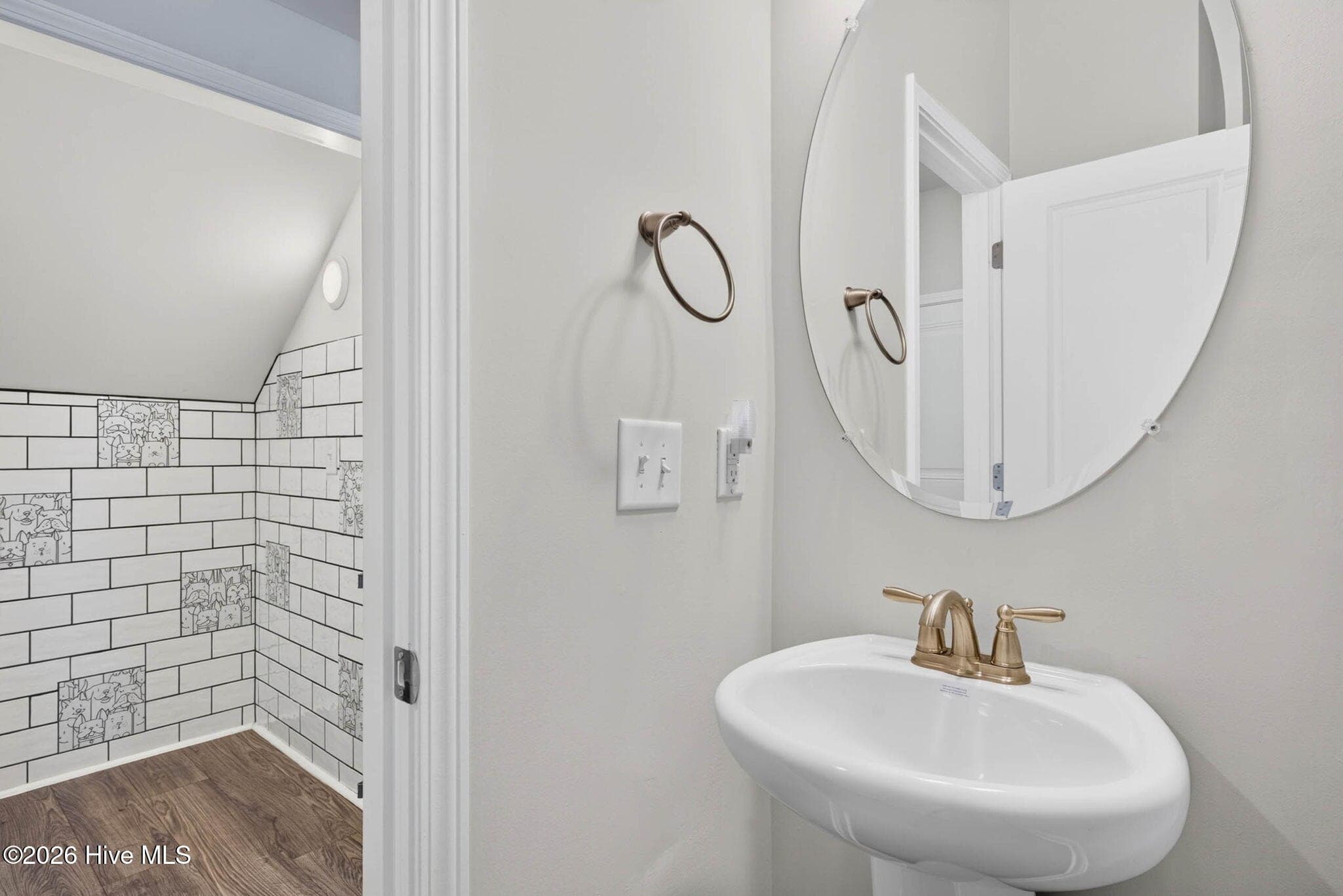 The stylish powder room features a pedestal sink, round mirror, and decorative tile accent wall. - 139 Eagle Claw Drive, Calabash, NC 28467