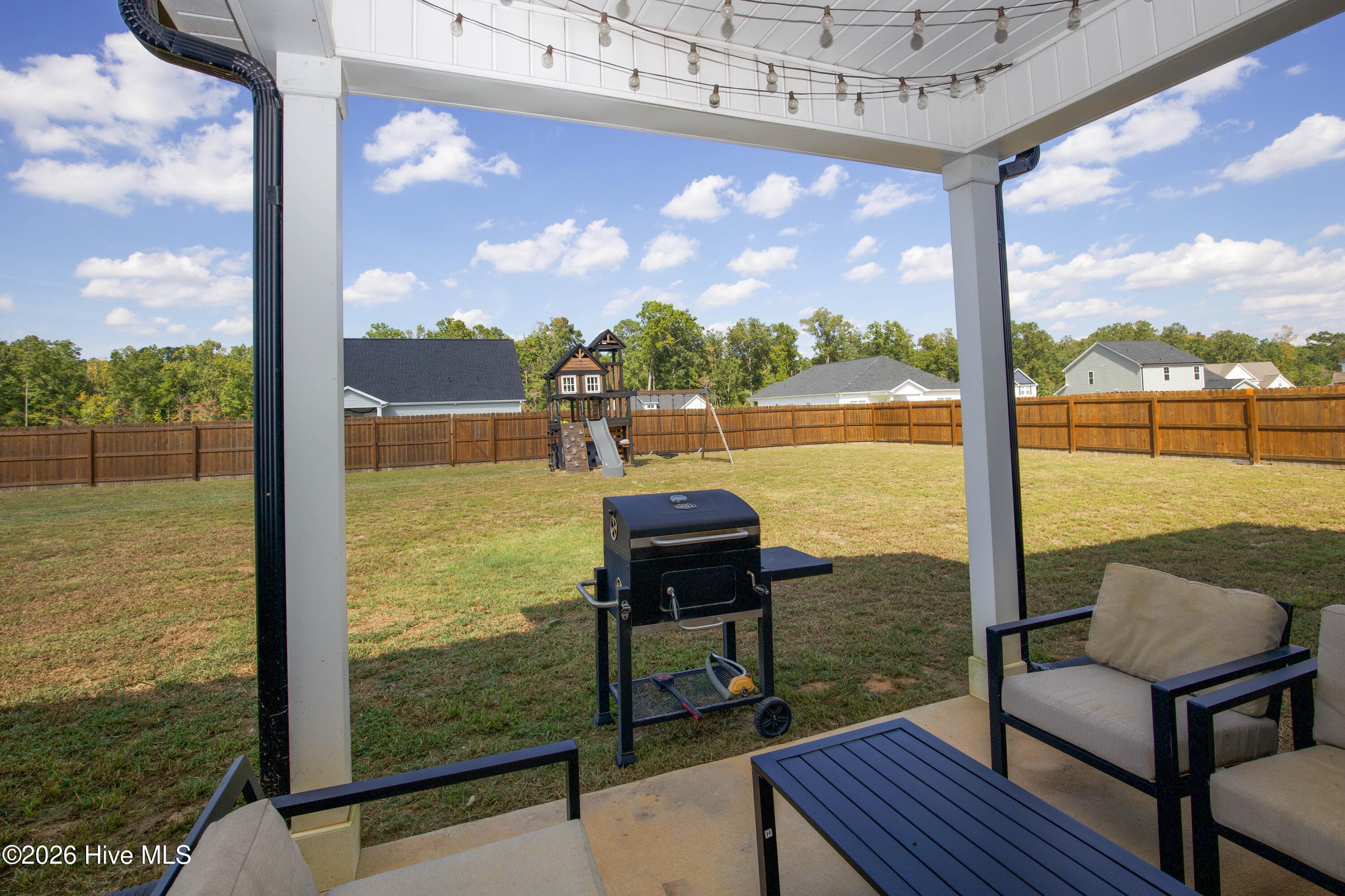 This patio view shows the full width of the backyard, with the fence running along the property line and the playground equipment set near the back. The existing playground equipment conveys with the property. The open lawn between the patio and the fence leaves room for gardening, outdoor games, or entertaining. - 221 Vega Lane, Linden, NC 28356