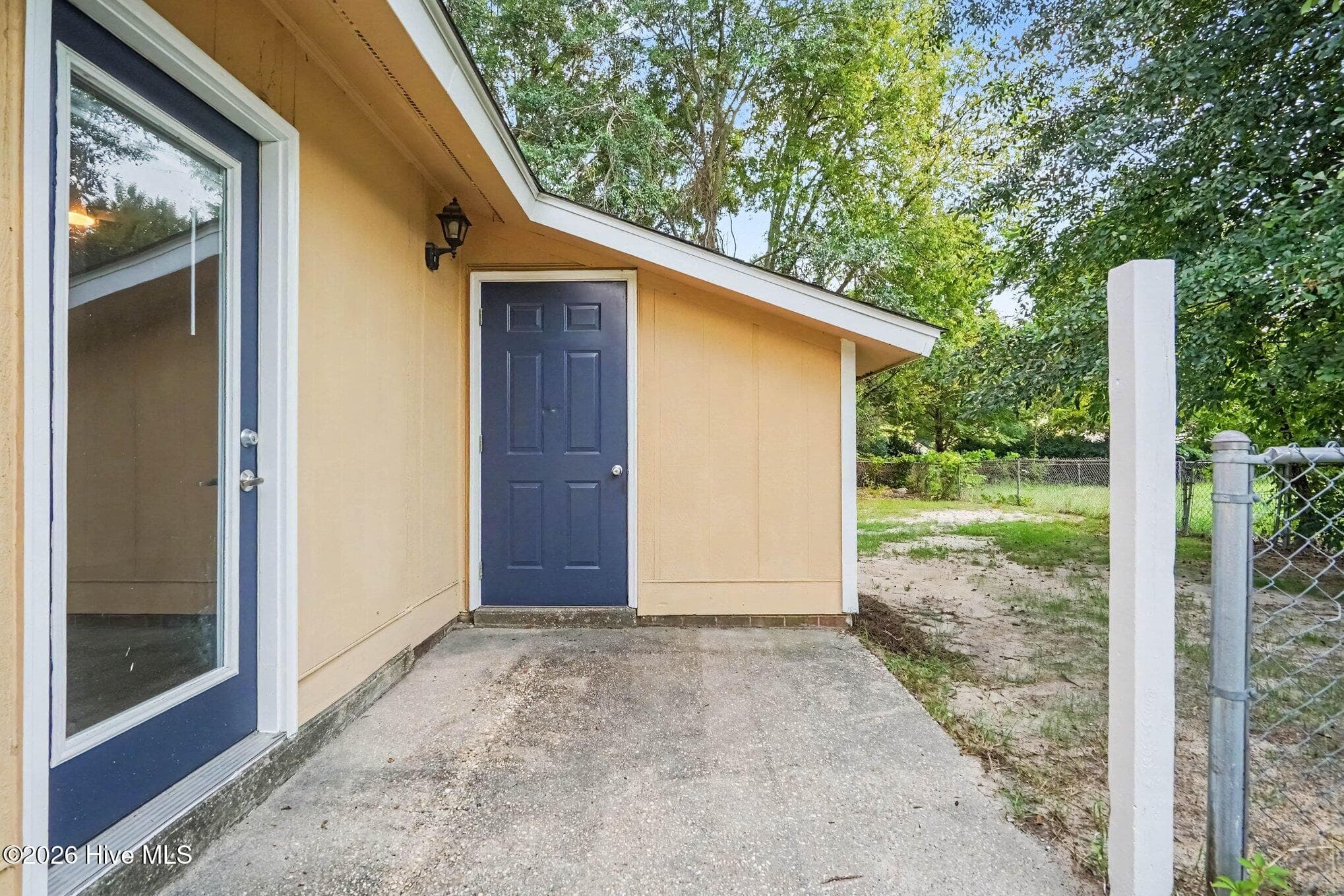 Private concrete patio space off the primary suite, complete with glass door access, exterior storage shed entry, and peaceful views of the shaded side yard. - 108 Deerfield Drive, Spring Lake, NC 28390