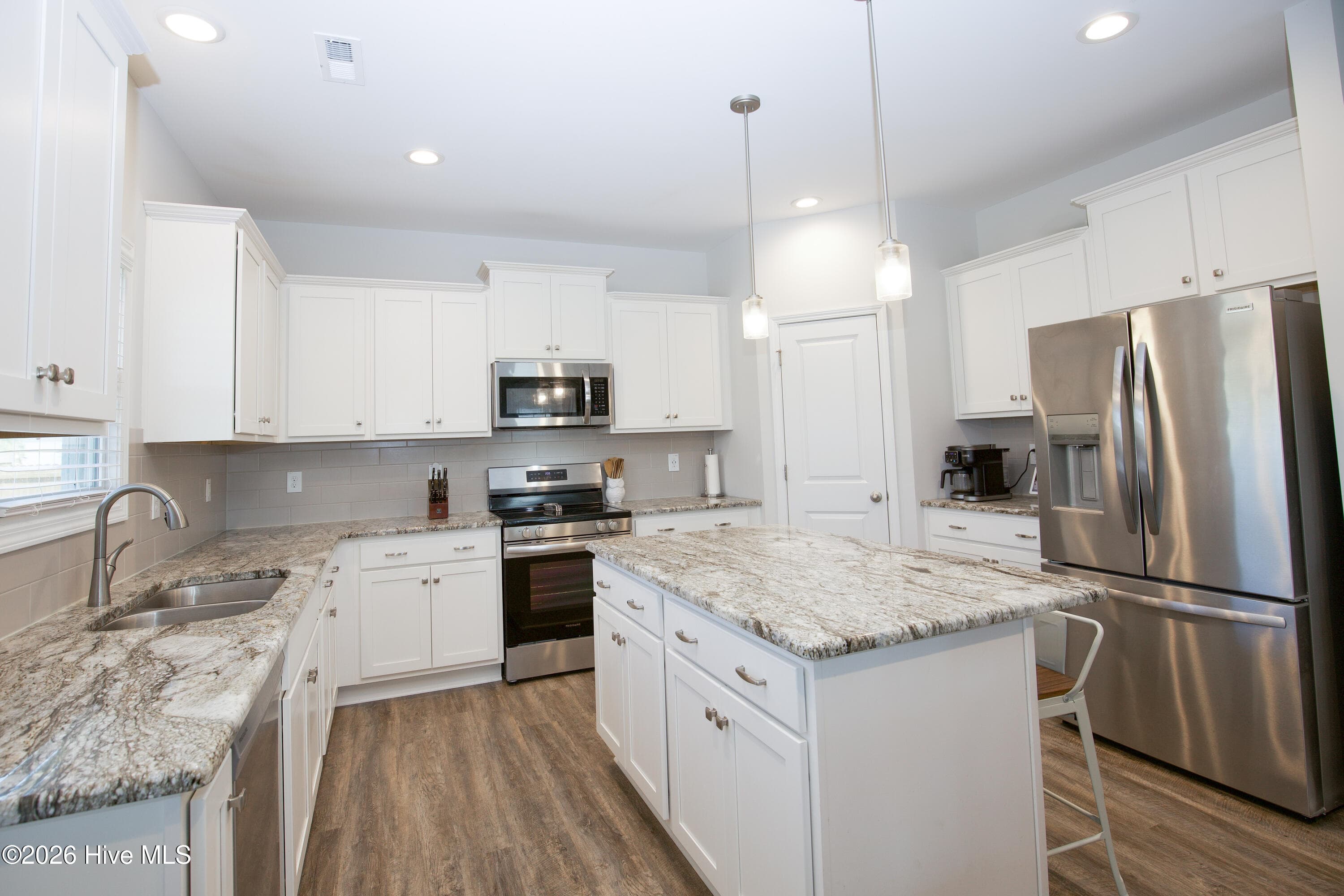 The kitchen is laid out with white shaker-style cabinetry on two walls and a large island in the center, giving you plenty of counter space for meal prep. Granite countertops, a tile backsplash, and pendant lights over the island tie the space together. The stainless range, over-range microwave, and dishwasher are part of the kitchen's finished look, and the refrigerator conveys with the home. - 221 Vega Lane, Linden, NC 28356