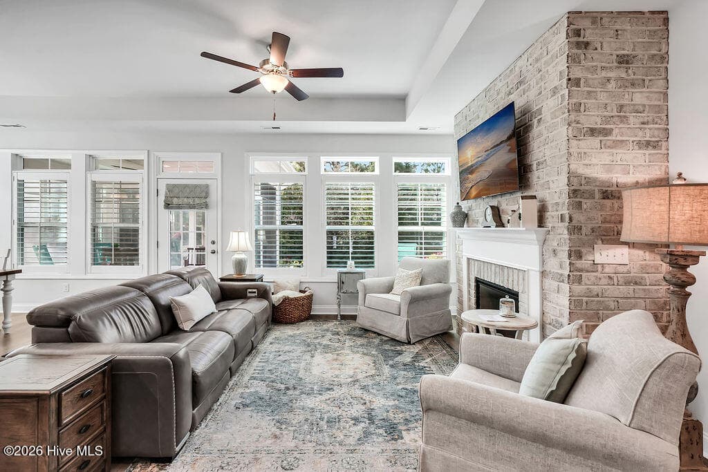 The living area is beautifully drenched in sunlight thanks to a bank of large, energy-efficient Low-E windows. Outfitted with custom plantation blinds, these windows allow for an easy transition between indoor and outdoor spaces and add an air of southern coastal charm to the neutral Scandi-meets-seaside color palette. A tray ceiling and an electric fireplace with custom brick surround complete this bright and open space. - 142 Rice Marsh Way, Wilmington, NC 28412