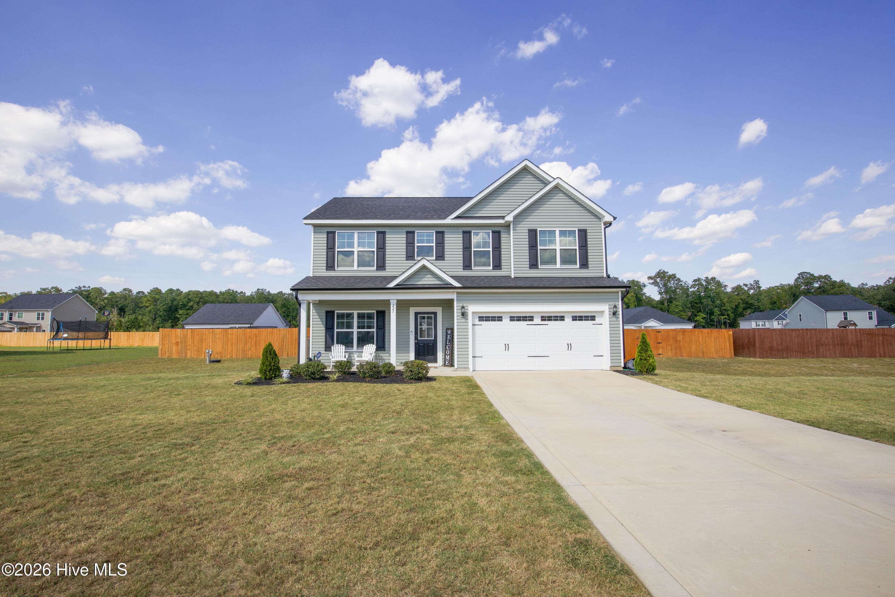 Viewed from the driveway, the home's attached two-car garage faces the street with a carriage-style door and windows across the top. The long concrete driveway provides room for additional parking in front of the garage. Inside, the garage includes built-in overhead storage compartments that convey with the home, adding space for bins and seasonal items. - 221 Vega Lane, Linden, NC 28356
