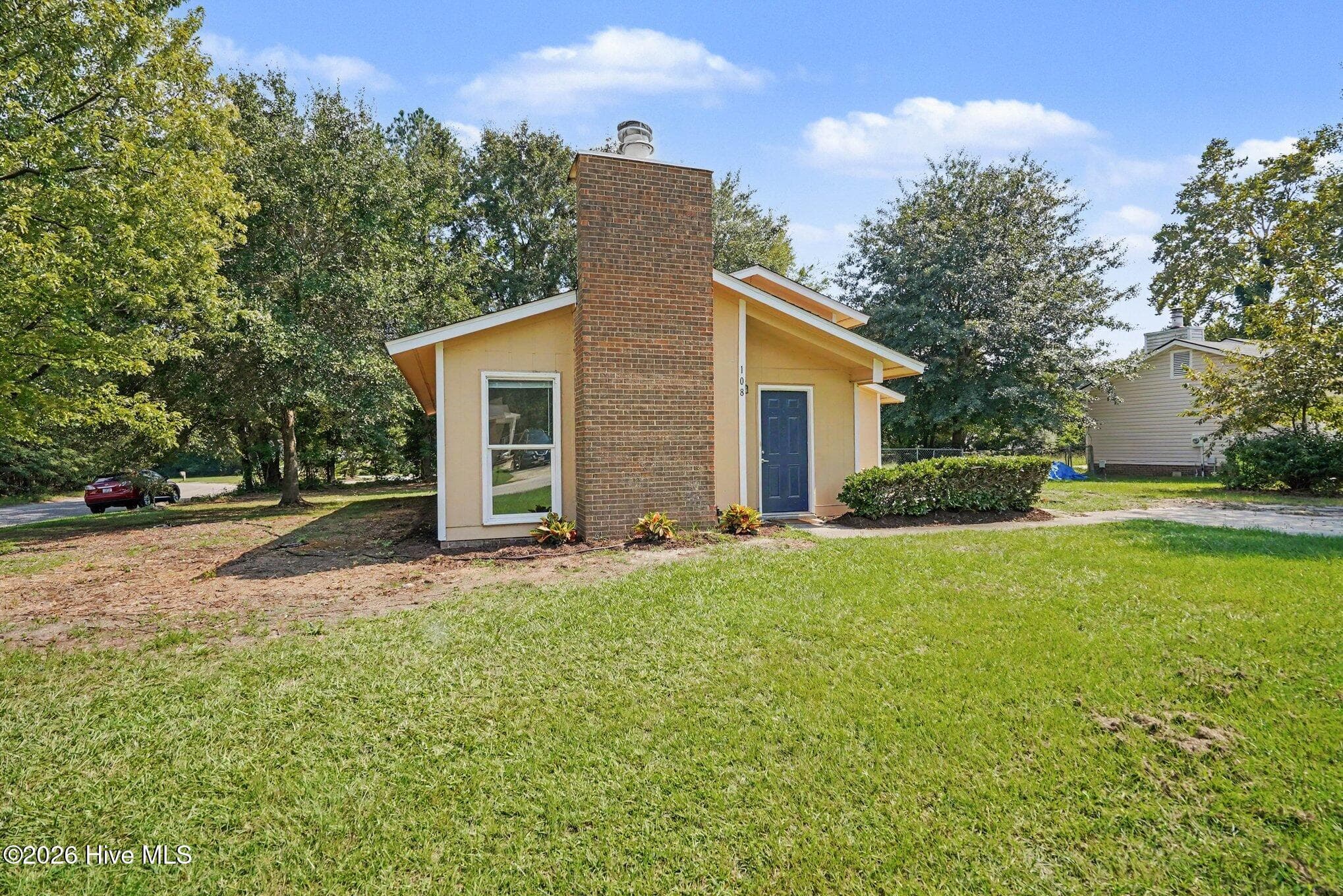 Situated on a corner lot, showcasing modern style architectural rooflines, a prominent brick chimney feature, low-maintenance landscaping, and a welcoming entryway. - 108 Deerfield Drive, Spring Lake, NC 28390