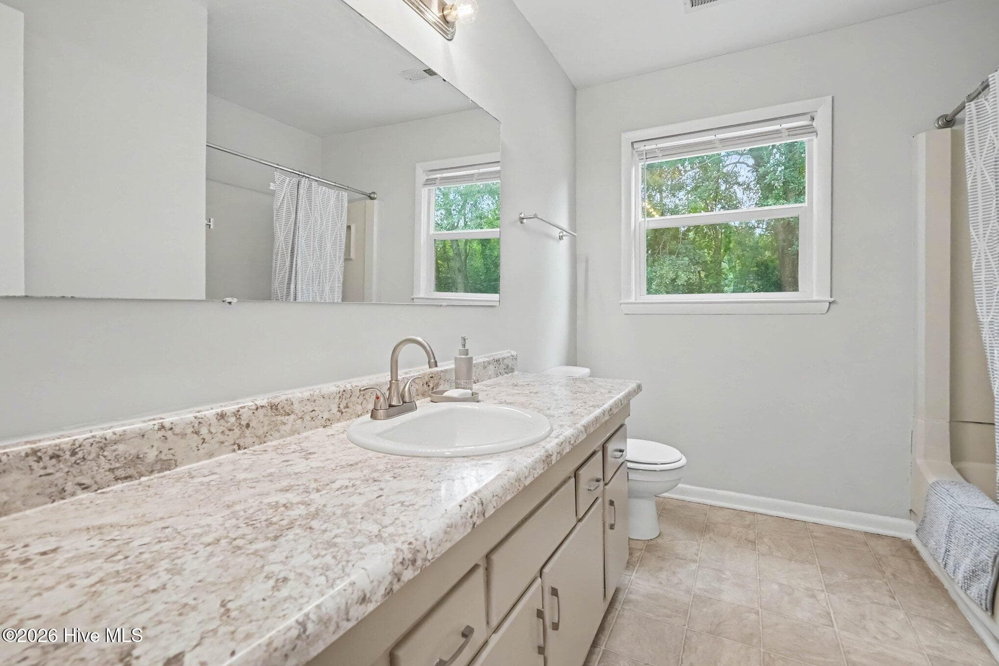 Full secondary bathroom featuring an extended vanity with abundant counter space and storage, large mirror, shower/tub combination, and a bright window offering natural light. - 108 Deerfield Drive, Spring Lake, NC 28390