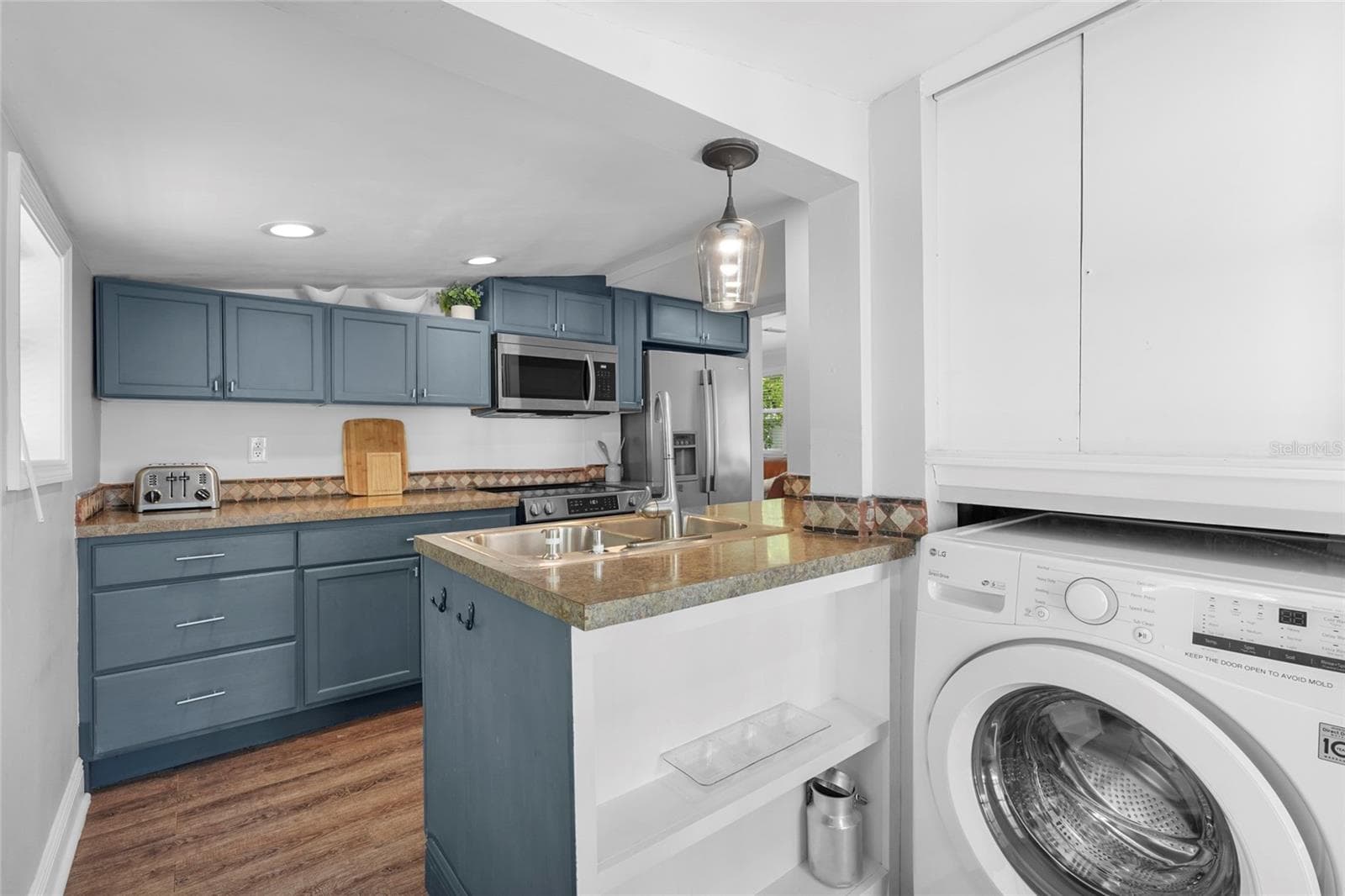 Functional Kitchen Pass-Through – A peek-through window into the laundry area, floating shelves, and updated light fixtures add thoughtful touches to this practical kitchen design. - 2705 2ND AVE W, BRADENTON