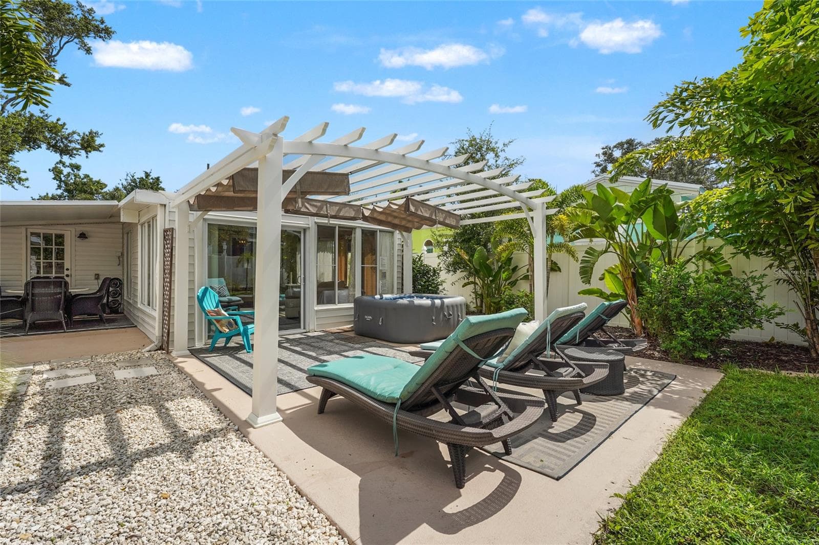 ?Backyard Bliss – Lounge poolside-style on this sun-soaked patio with multiple chaises, outdoor rugs, and a stylish white pergola, seamlessly extending from the Florida room. - 2705 2ND AVE W, BRADENTON