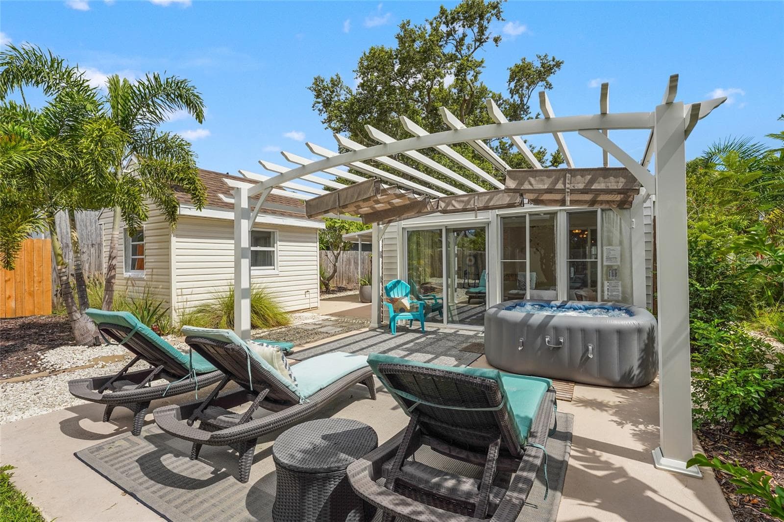 ?Backyard Bliss – Lounge poolside-style on this sun-soaked patio with multiple chaises, outdoor rugs, and a stylish white pergola, seamlessly extending from the Florida room. - 2705 2ND AVE W, BRADENTON