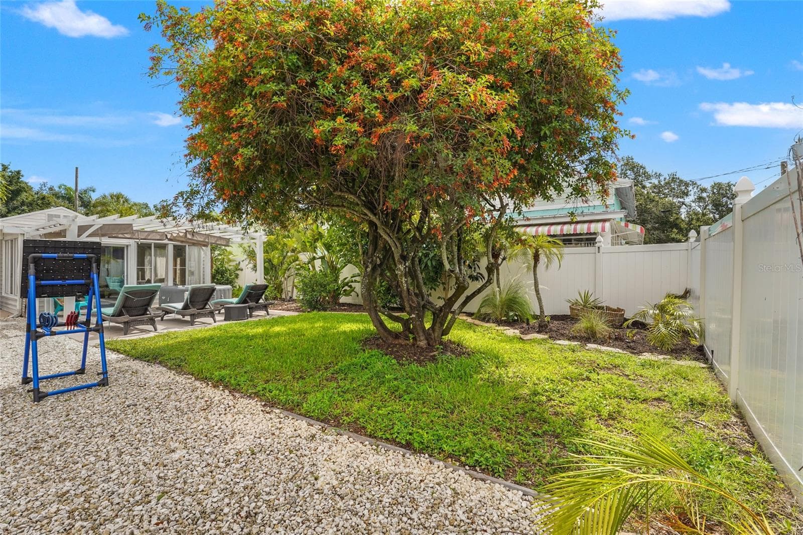 Relax + Play – This backyard is made for fun with a sunny lawn, lounging area, and even room for games like cornhole or target toss, all framed by tropical foliage and a white privacy fence. - 2705 2ND AVE W, BRADENTON