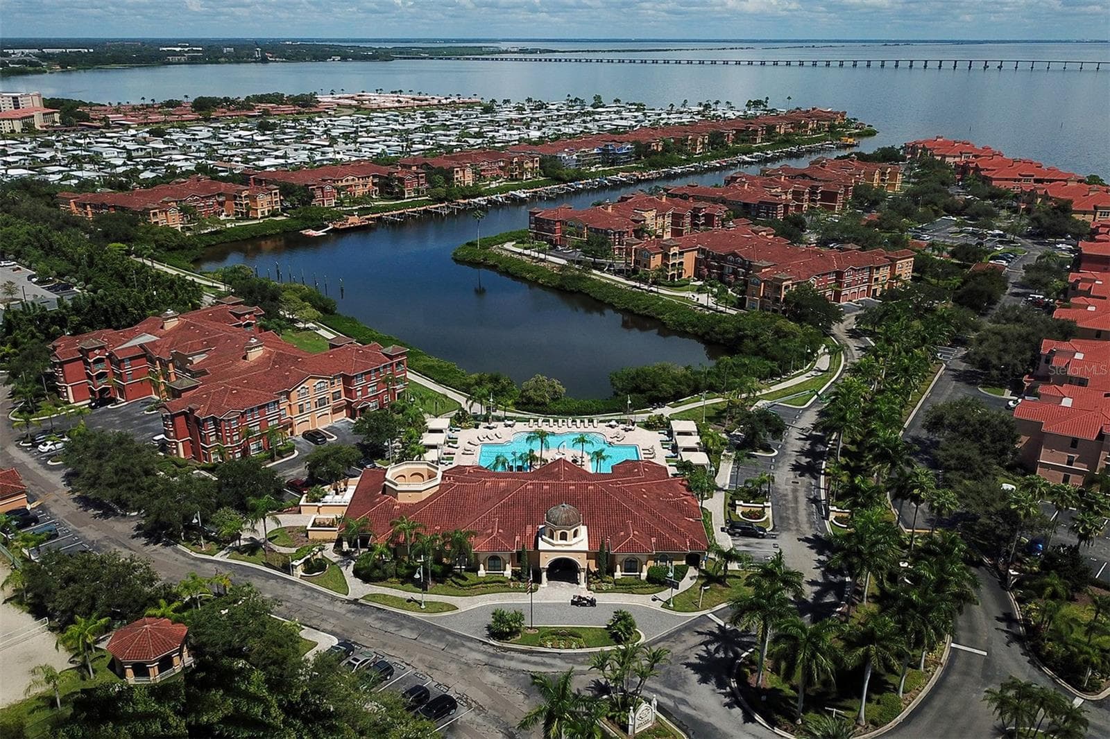 Aerial view of the front of The Grand Bellagio clubhouse, pool and bayou/inlet out into Old Tampa Bay - 2757 VIA CIPRIANI #1114A, CLEARWATER