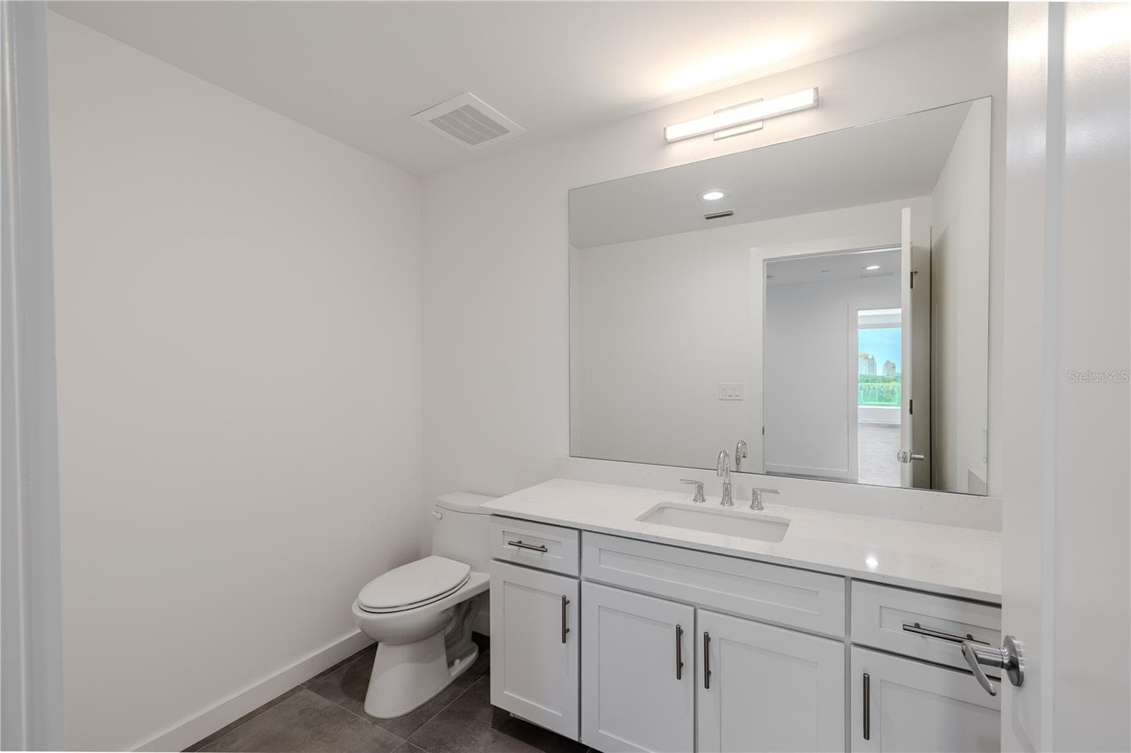 Guest bathroom #4 continues the home’s clean, modern aesthetic with a bright, streamlined design. The vanity features shaker-style cabinetry with brushed nickel hardware, a sleek quartz countertop, and an undermount sink complemented by polished chrome fixtures.A large, framed mirror and contemporary lighting create a well-lit, sophisticated atmosphere, while neutral tile flooring adds warmth and durability. Conveniently located near the main living areas and guest quarters, this bathroom offers both function and style — ideal for guests or everyday use. - 920 N OSCEOLA AVE #703, CLEARWATER