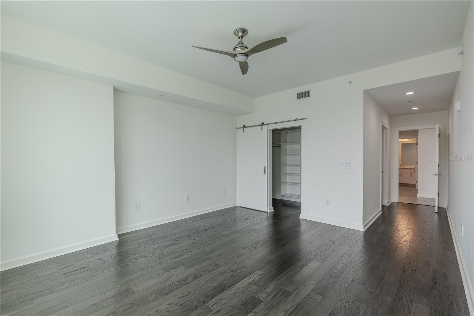 This inviting second bedroom features rich hardwood floors, recessed lighting, and a sleek ceiling fan that adds a touch of modern style. A sliding barn door opens to a custom closet with built-in shelving for organized storage. The room connects conveniently to an en-suite bath - 920 N OSCEOLA AVE #703, CLEARWATER