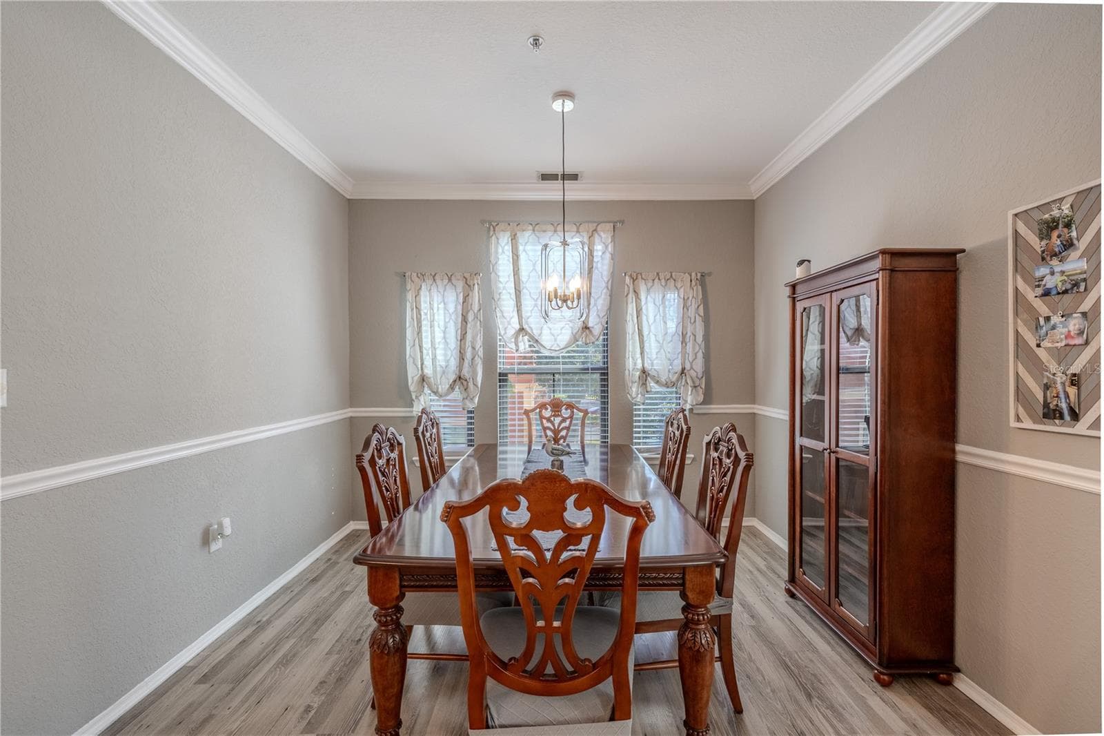An elegant dining room features crown molding, chair rail detailing, wide-plank laminate flooring, and a modern pendant light, creating a refined space perfect for hosting gatherings and formal meals. - 2738 VIA TIVOLI #220B, CLEARWATER