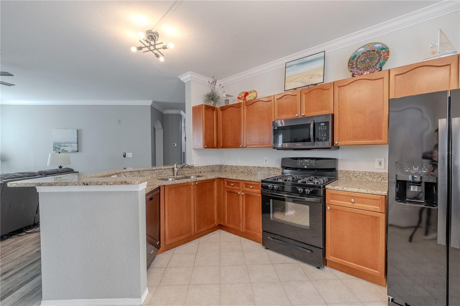 Bright, open kitchen featuring warm wood cabinetry, granite countertops, and black appliances, with a breakfast bar that overlooks the living area for easy entertaining. - 2738 VIA TIVOLI #220B, CLEARWATER