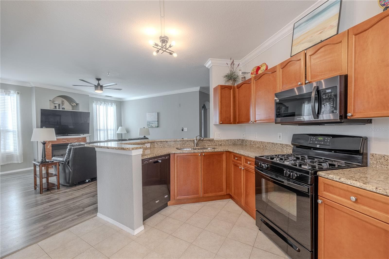 From the kitchen’s granite breakfast bar, the open living and dining areas unfold with crown molding, abundant natural light, and a cozy fireplace that anchors the inviting open-concept layout. - 2738 VIA TIVOLI #220B, CLEARWATER