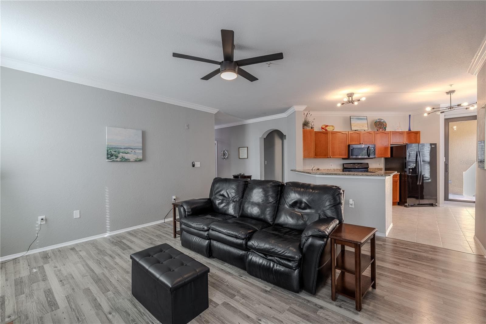 Spacious open living area with updated flooring, crown molding, and a modern ceiling fan, offering a seamless flow to the kitchen with a breakfast bar—ideal for relaxing or entertaining. - 2738 VIA TIVOLI #220B, CLEARWATER
