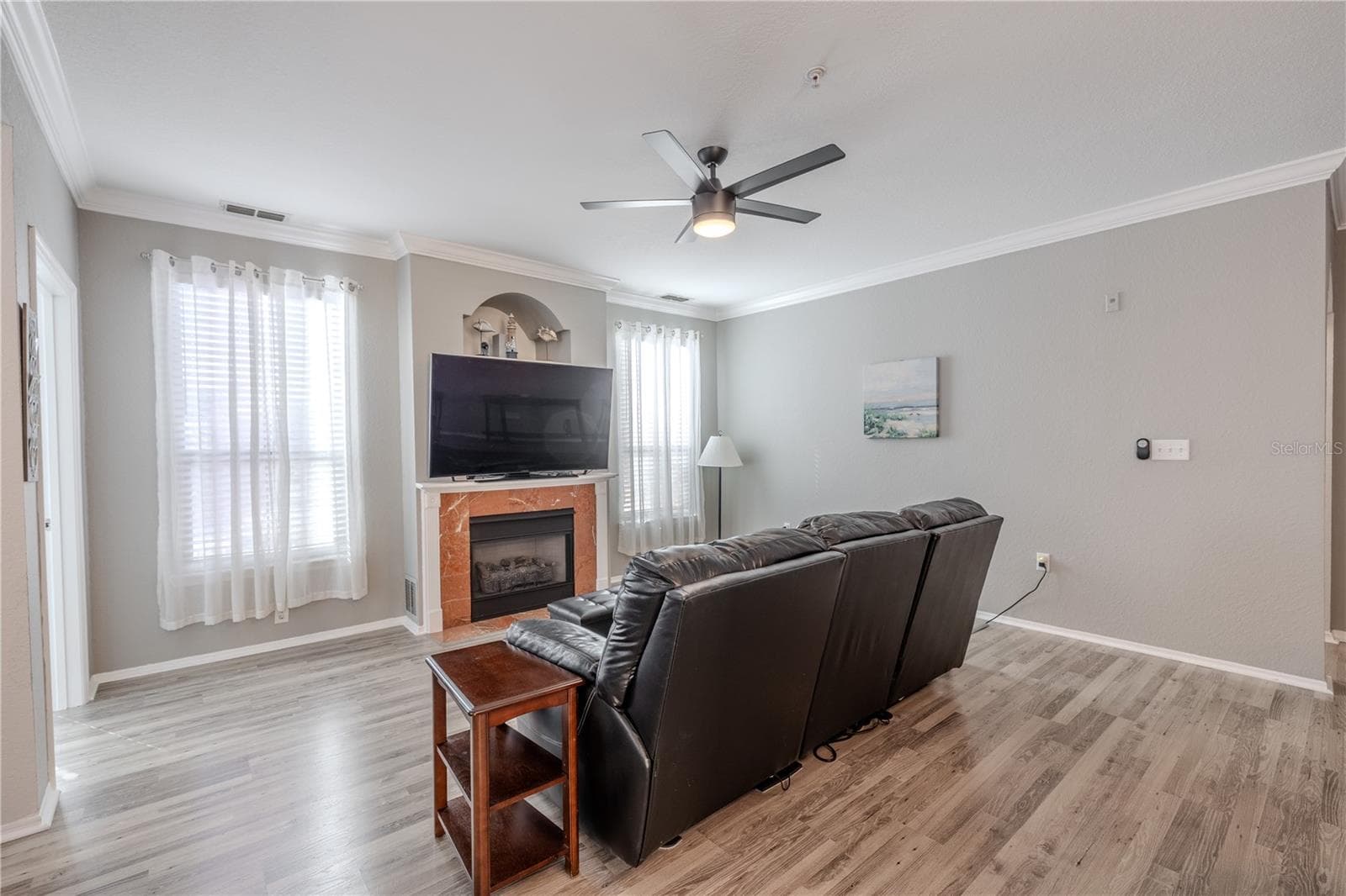 This inviting living area is anchored by a gas fireplace with a classic mantle and decorative niche above, flanked by tall windows with sheer curtains that fill the space with soft, natural light. - 2738 VIA TIVOLI #220B, CLEARWATER