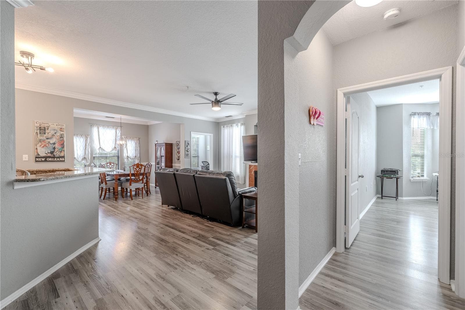 This view highlights the seamless flow from the open living and dining area into the private hallway leading to the bedrooms, showcasing the unit’s airy layout, cohesive flooring, and thoughtful separation of living and sleeping spaces. - 2738 VIA TIVOLI #220B, CLEARWATER