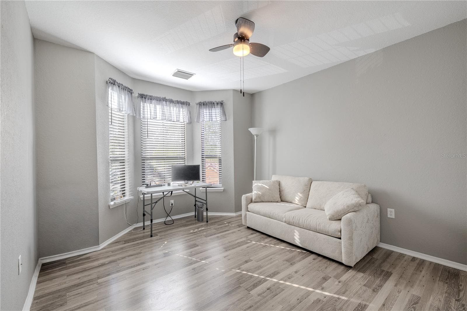 This bright second bedroom features multiple windows for natural light, neutral finishes, wood-look laminate flooring, and ample space to function comfortably as a guest room, home office, or flex space. - 2738 VIA TIVOLI #220B, CLEARWATER